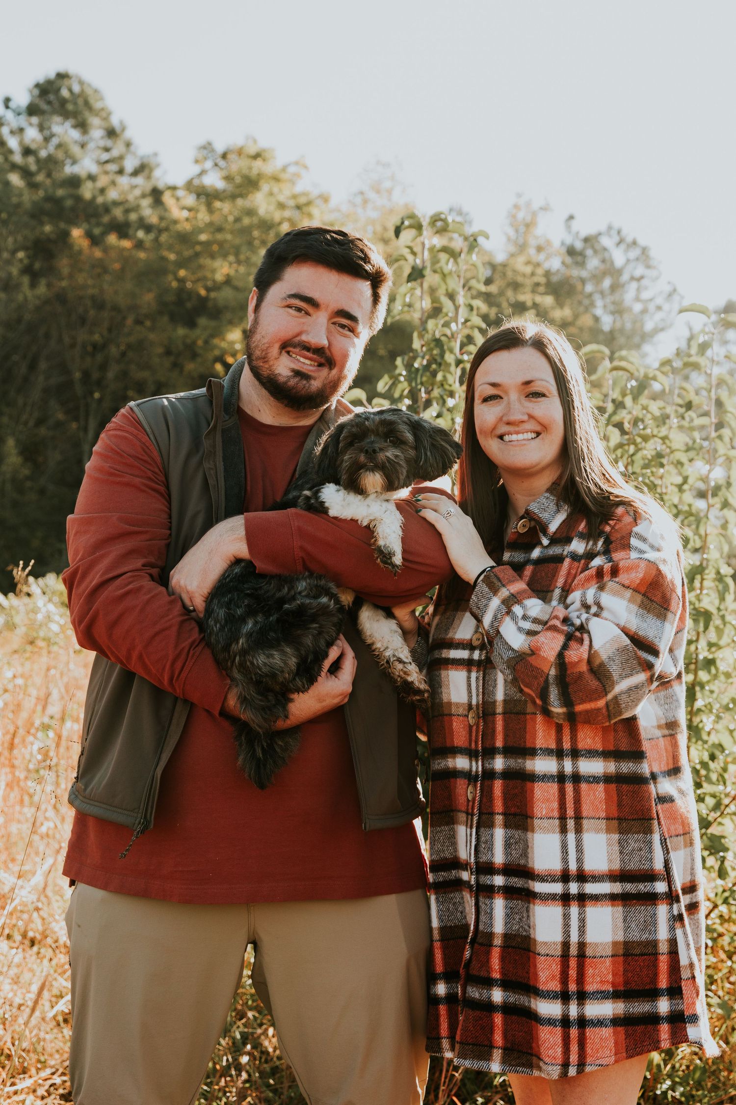 A couple poses with their small black dog during an outdoor autumn photoshoot.