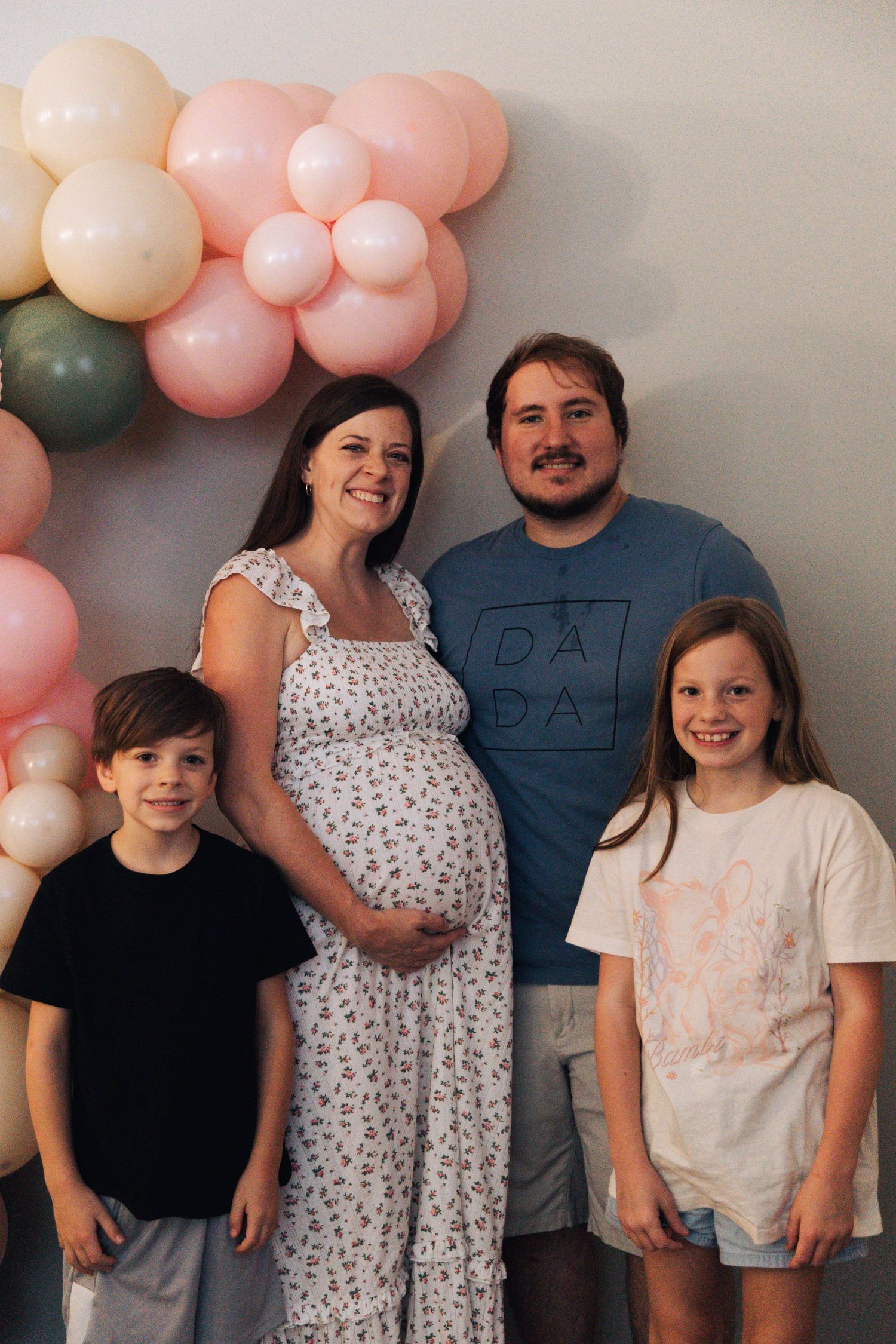 Happy family portrait against a wall decorated with pink and peach balloons.