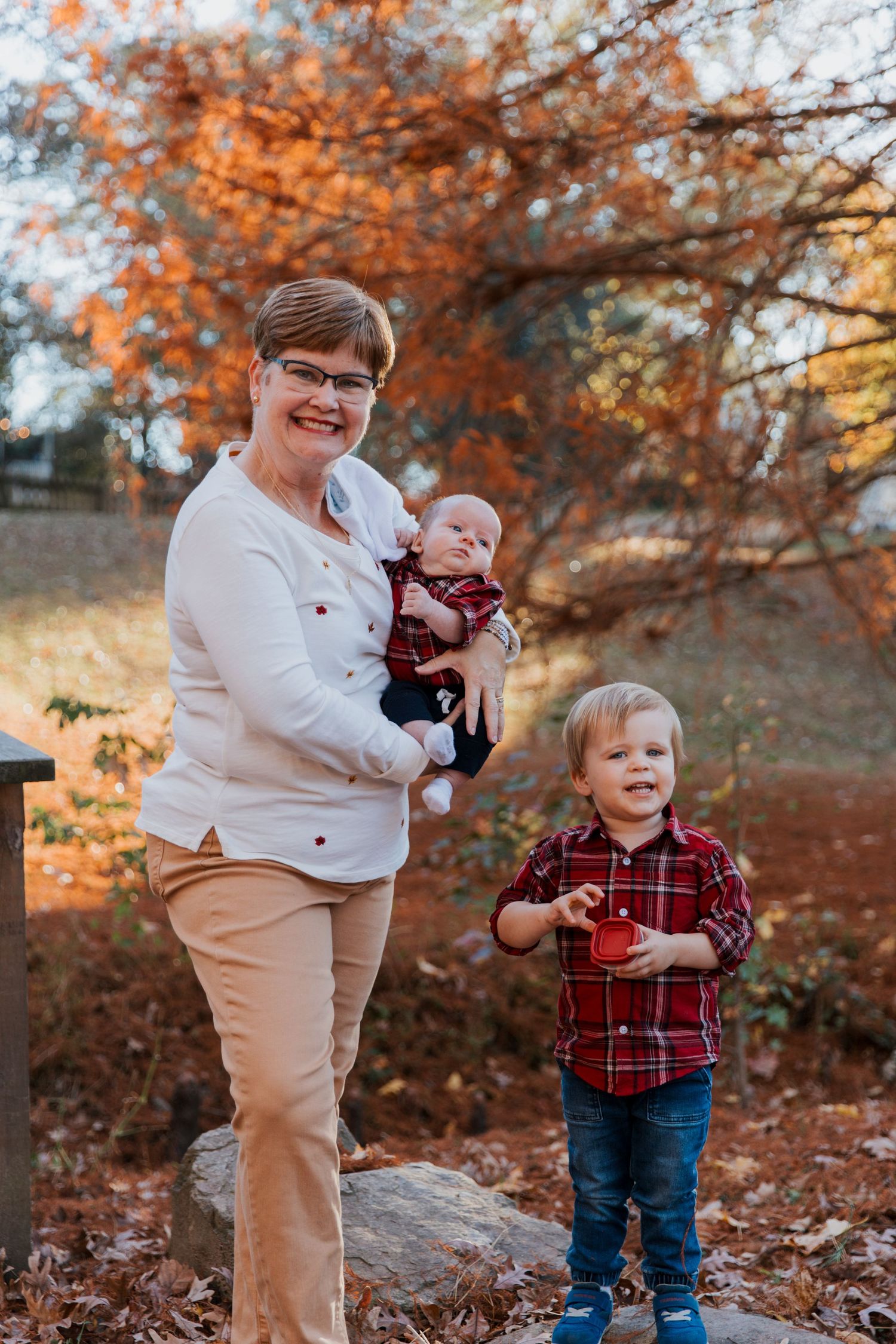 A family portrait in autumn featuring coordinating red plaid outfits among falling leaves.