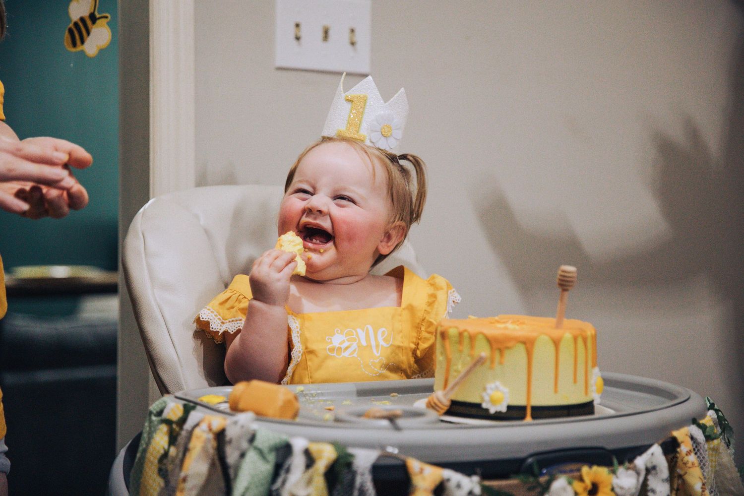 A baby in a high chair enthusiastically smashes and plays with yellow birthday cake during a cake smash photo session.