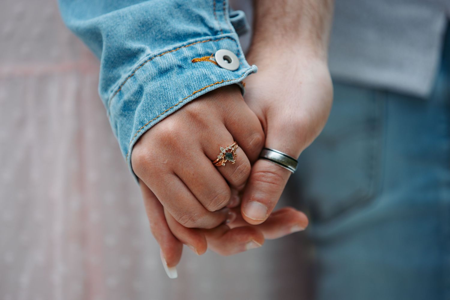 Close-up of hands wearing wedding rings against denim fabric.