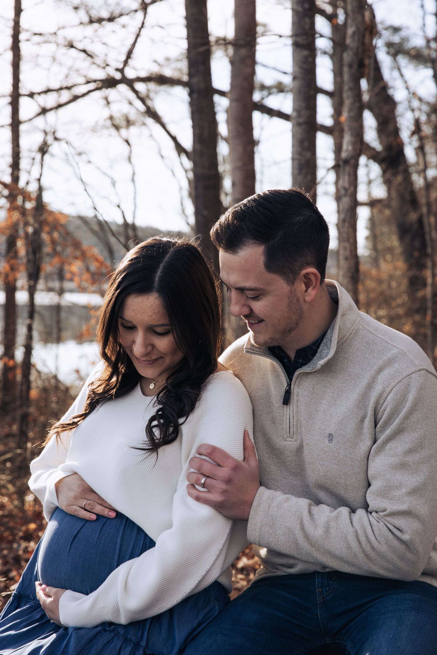 A couple in casual winter attire share intimate moments in a forest setting during a photo session.