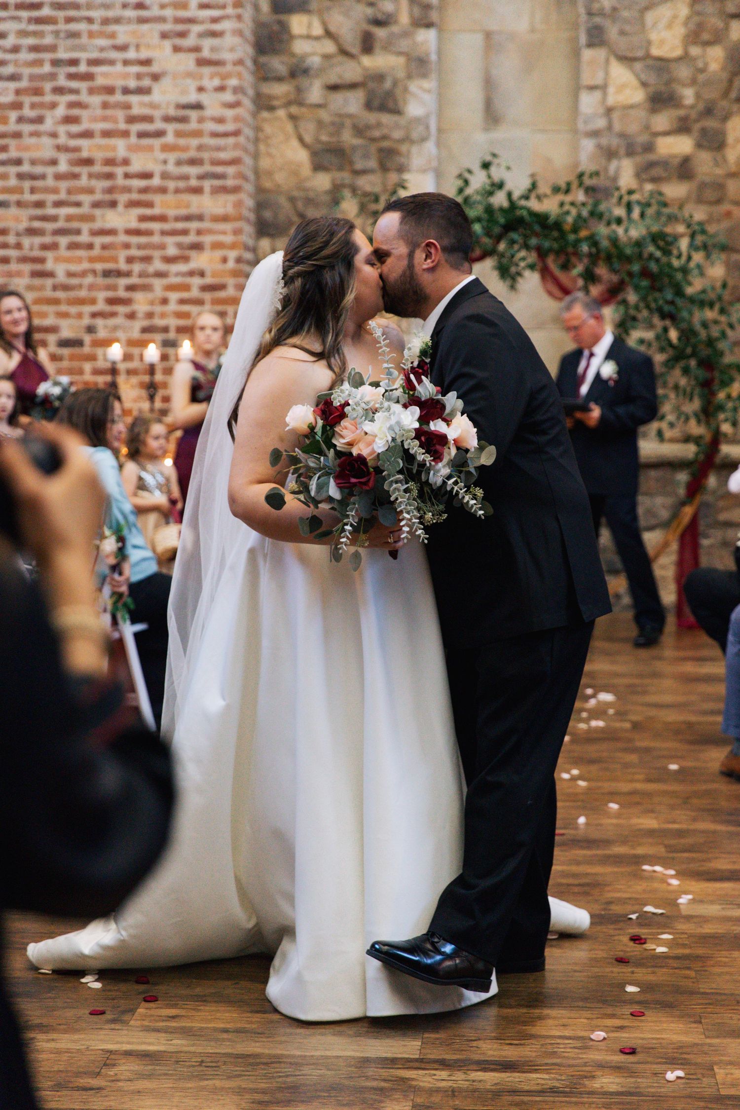 A wedding couple shares an intimate moment on a rustic wooden floor with brick walls.