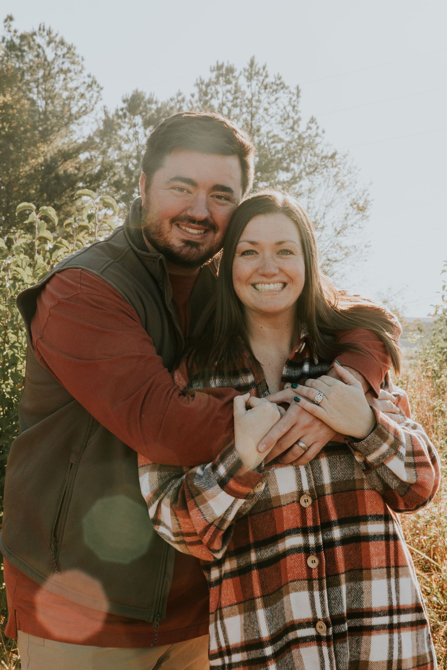 A couple shares a warm embrace outdoors on a sunny autumn day.