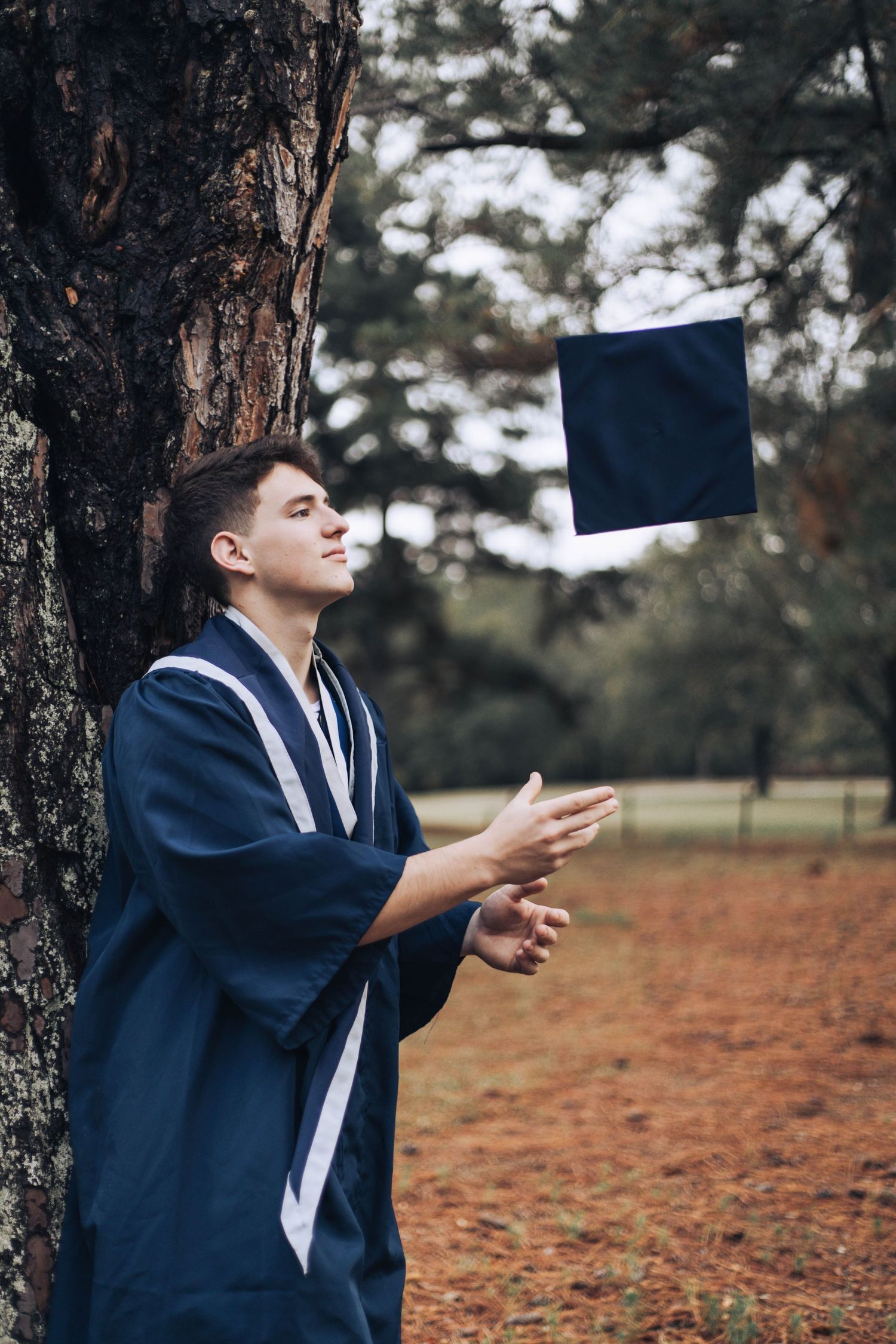 A series of photos showing someone in a navy graduation robe tossing a diploma in the air among autumn trees.