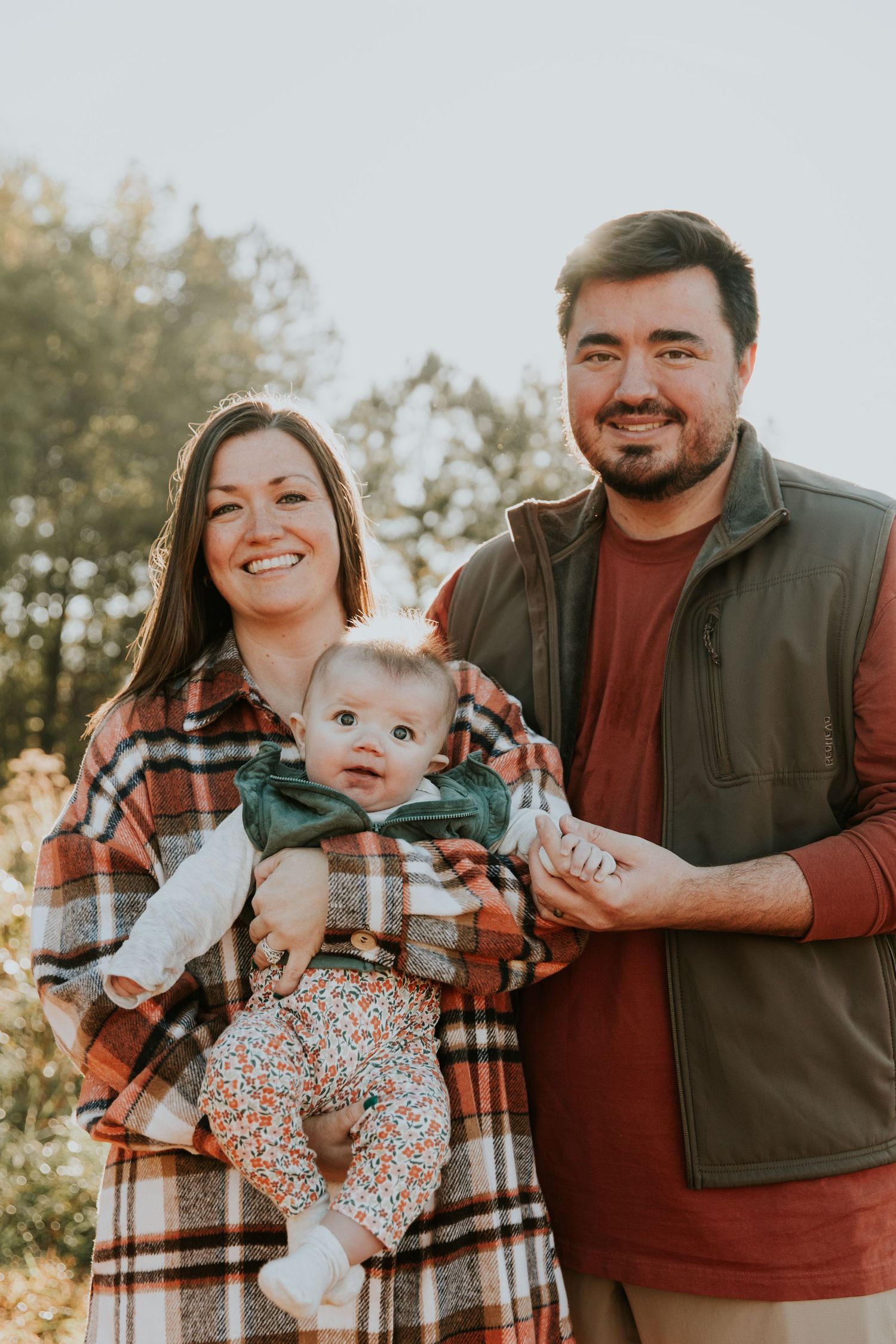 A family poses together in coordinating plaid and burgundy outfits during a golden hour outdoor photoshoot.
