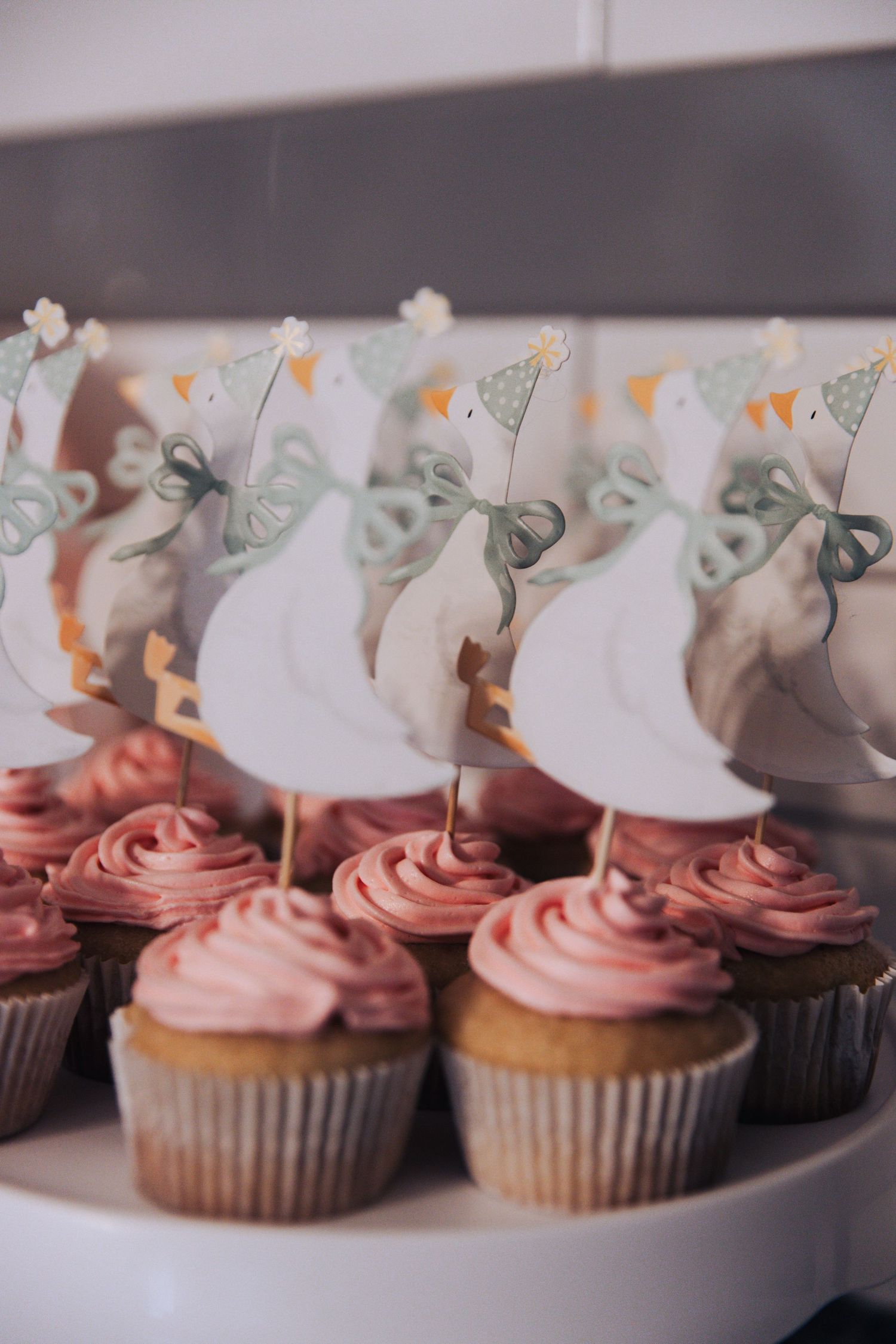 Pink frosted cupcakes decorated with white swan toppers arranged in a row on a display.