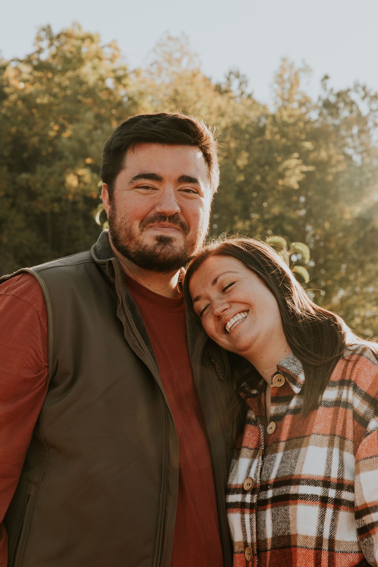 A couple laughs and embraces outdoors during a golden hour photoshoot in autumn.