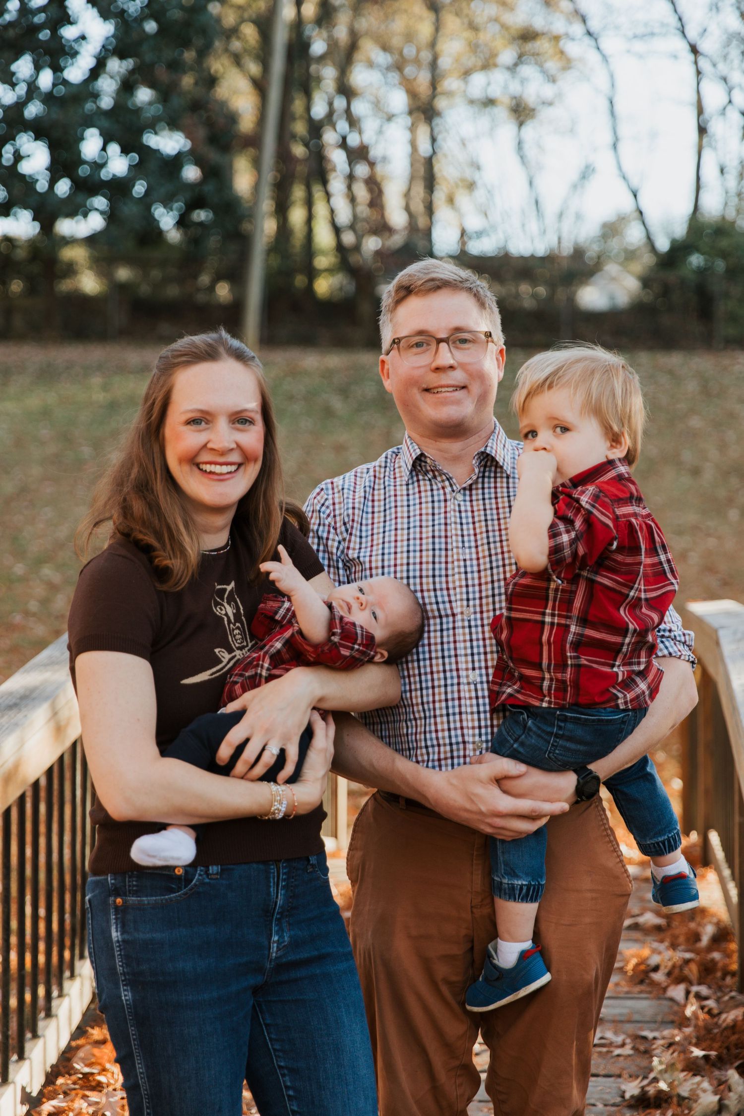 A family shares joyful moments together on a wooden walkway surrounded by fallen autumn leaves.