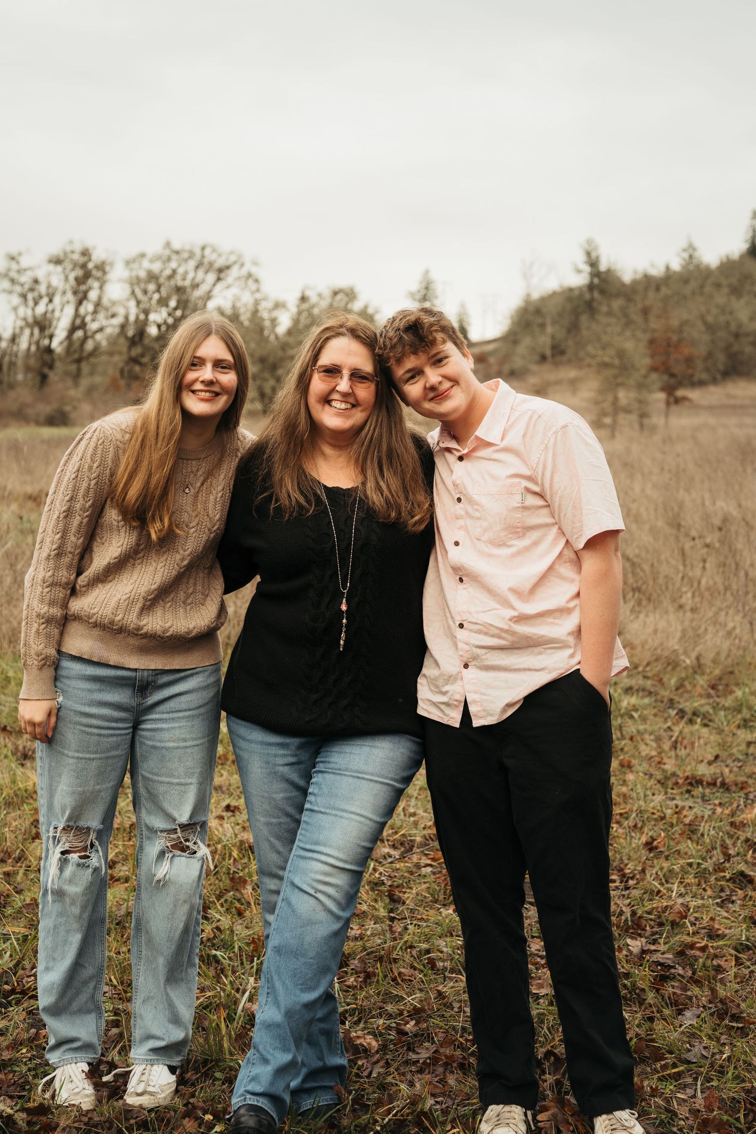 Three people in casual wear pose together in a field during autumn.