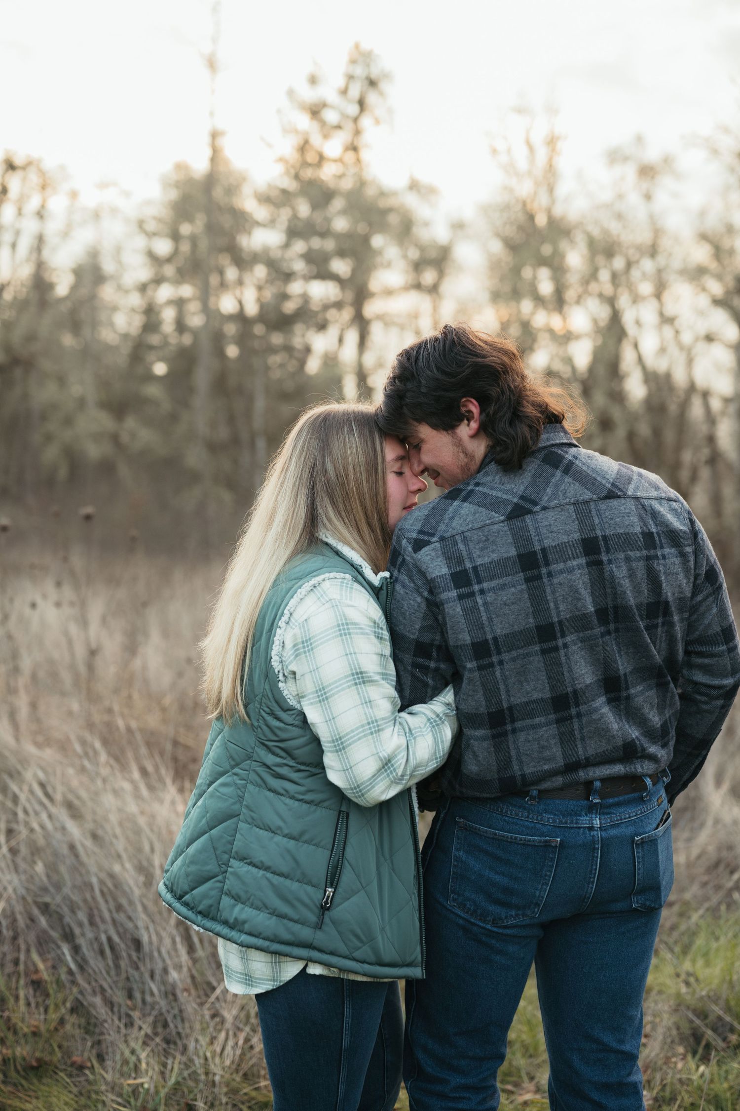 A couple in plaid and puffy jackets share an intimate moment in a misty autumn field.