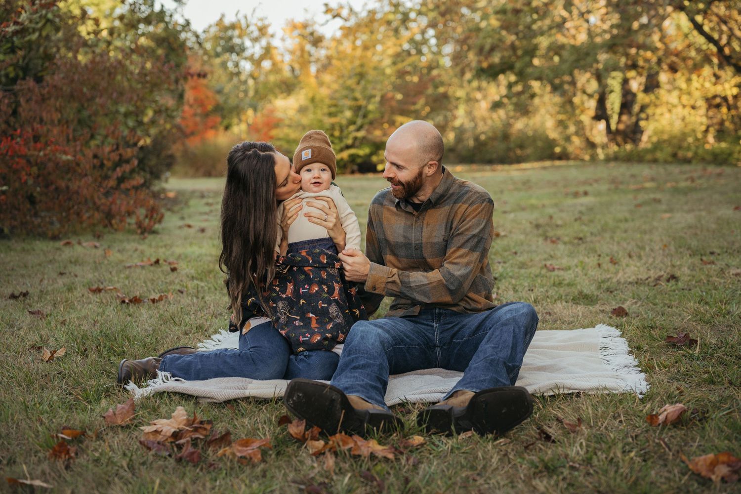 Family sits together on blanket during autumn outdoor photo session.