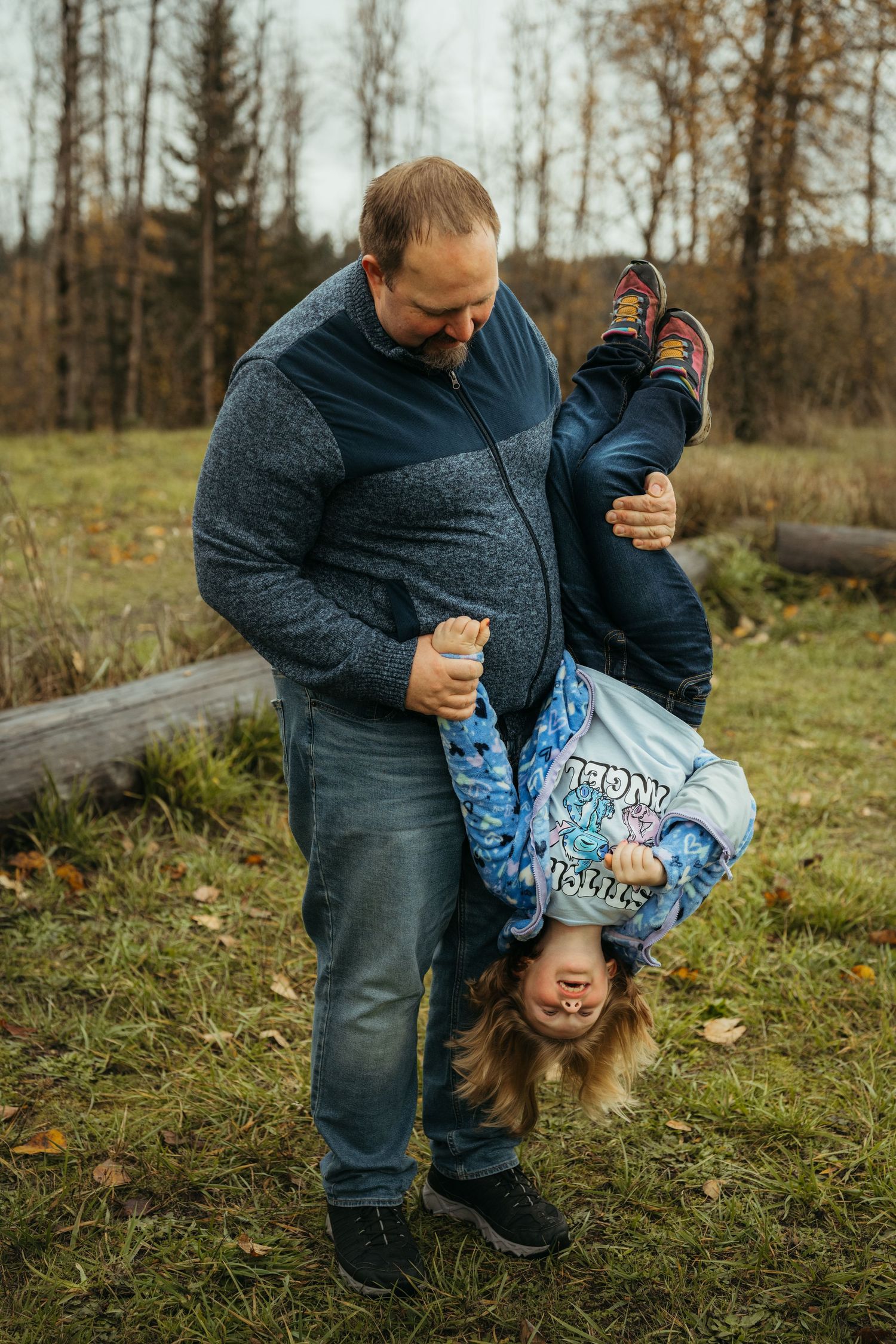 Playful moment captured as child is held upside down while wearing blue patterned jacket outdoors.