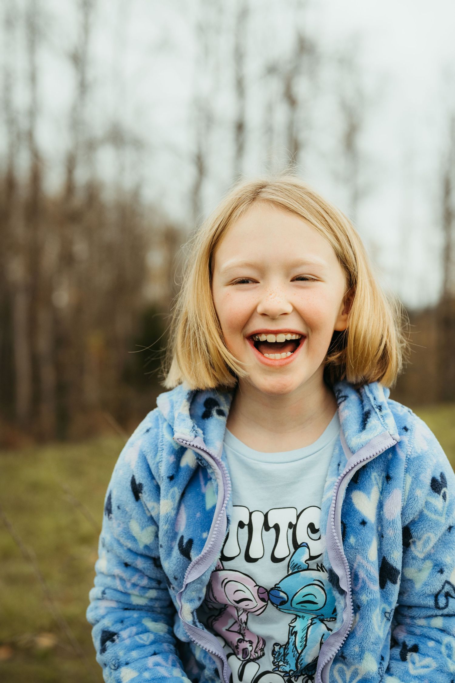Child wearing blue patterned hoodie laughing joyfully outdoors in autumn setting.