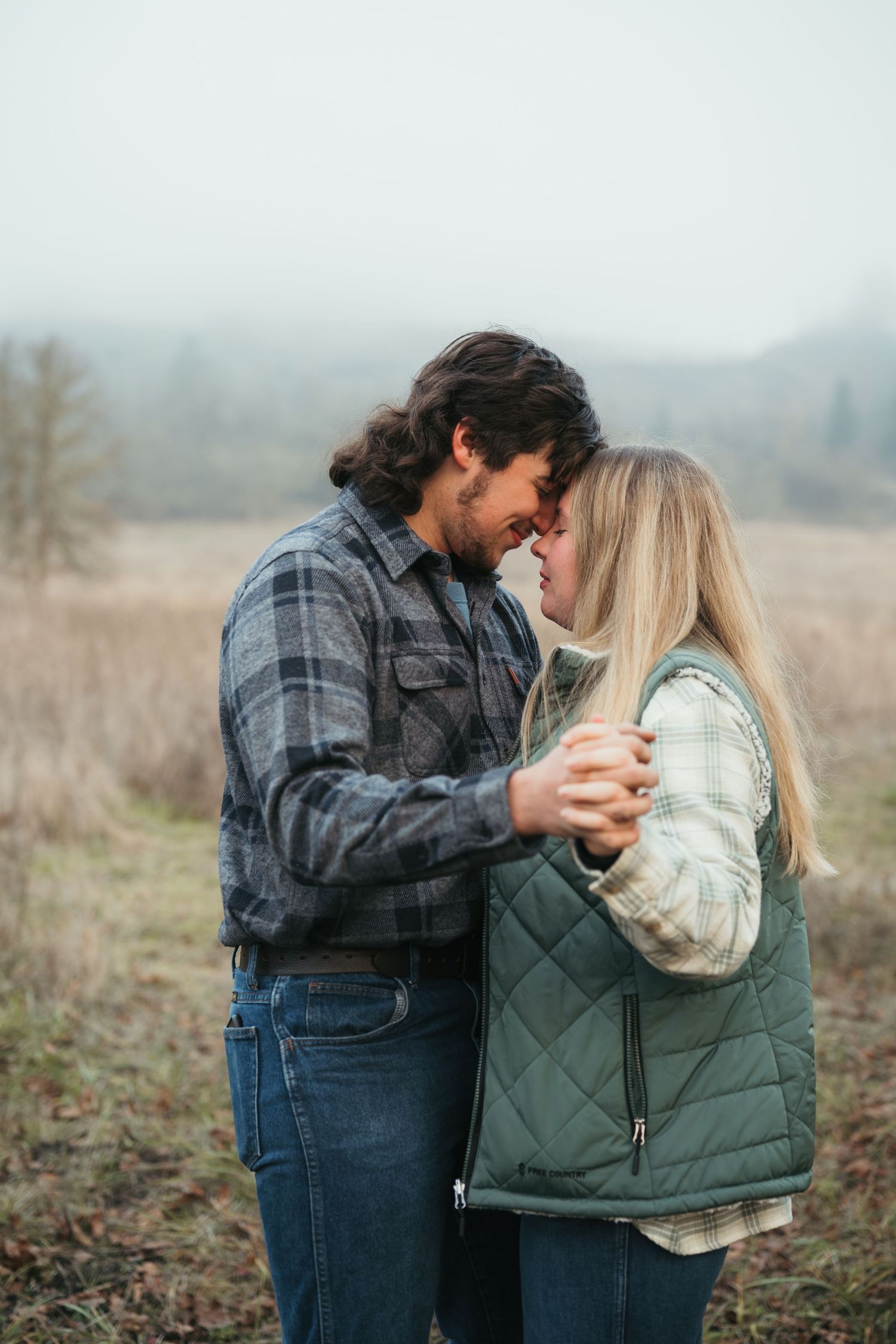 Romantic couple embracing in misty field wearing casual winter attire.