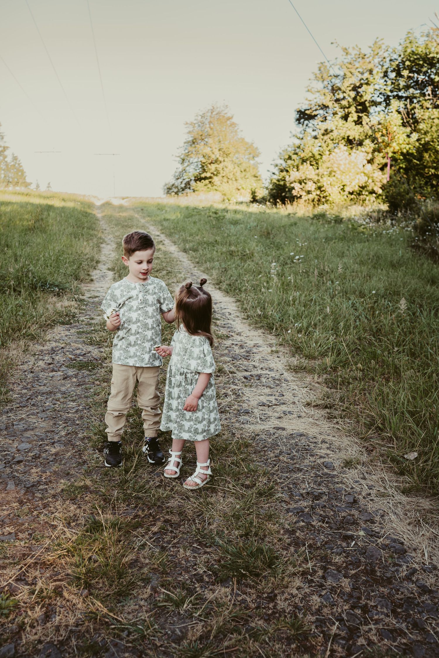 Two children in matching floral outfits stand close together on a rustic dirt path.