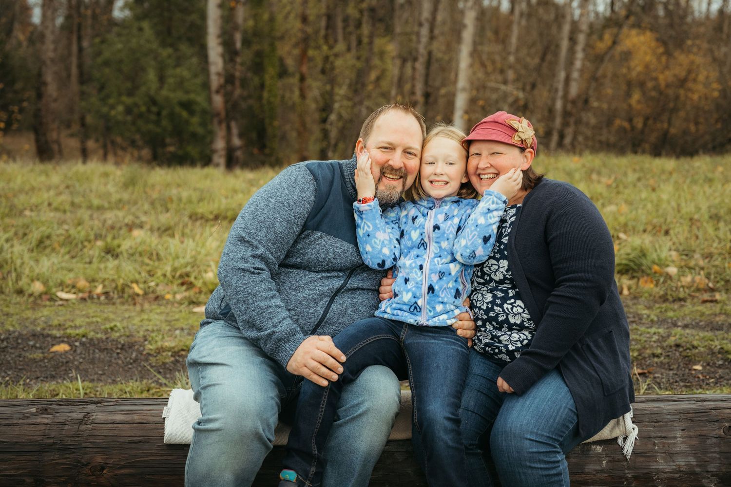 A family shares a joyful moment while sitting together on a wooden bench outdoors.