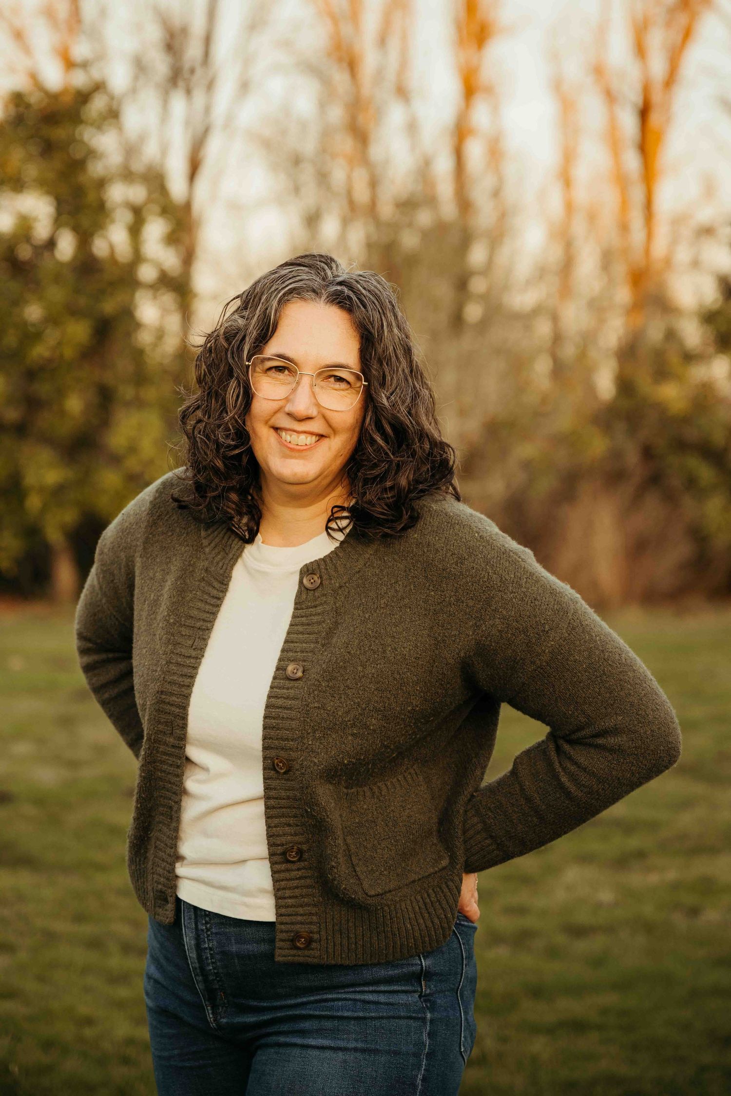 A person in a brown cardigan and white shirt poses outdoors during golden hour in a casual photo series.