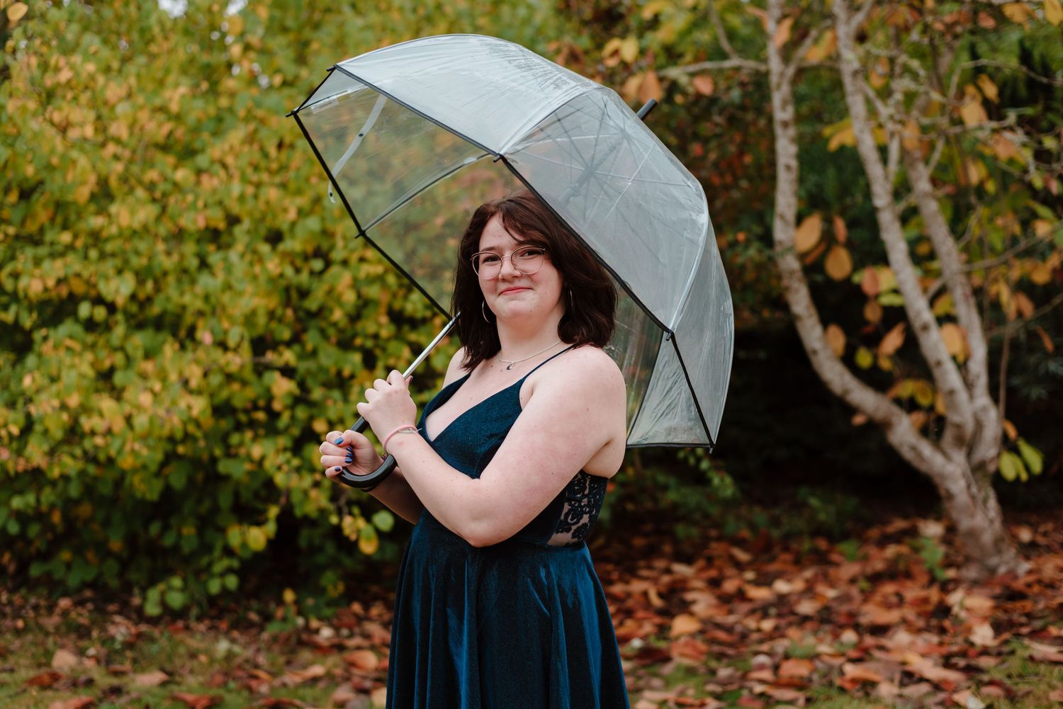 Person in a navy blue dress holds a clear umbrella while surrounded by autumn foliage.