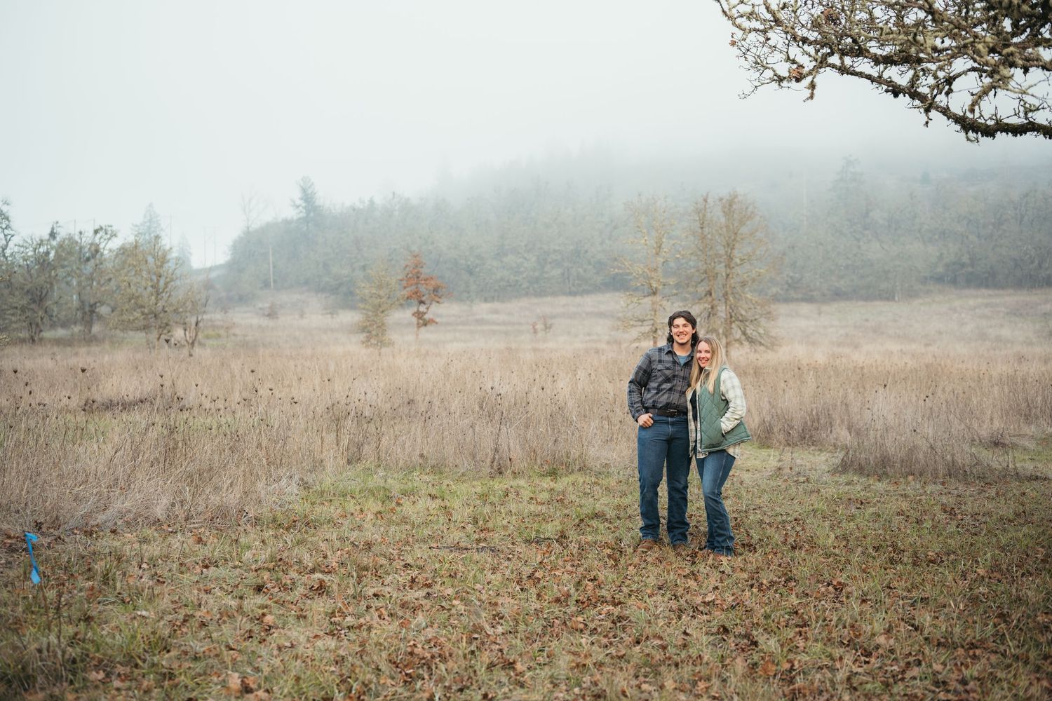 A couple stands together in a misty field during a moody outdoor photo session.