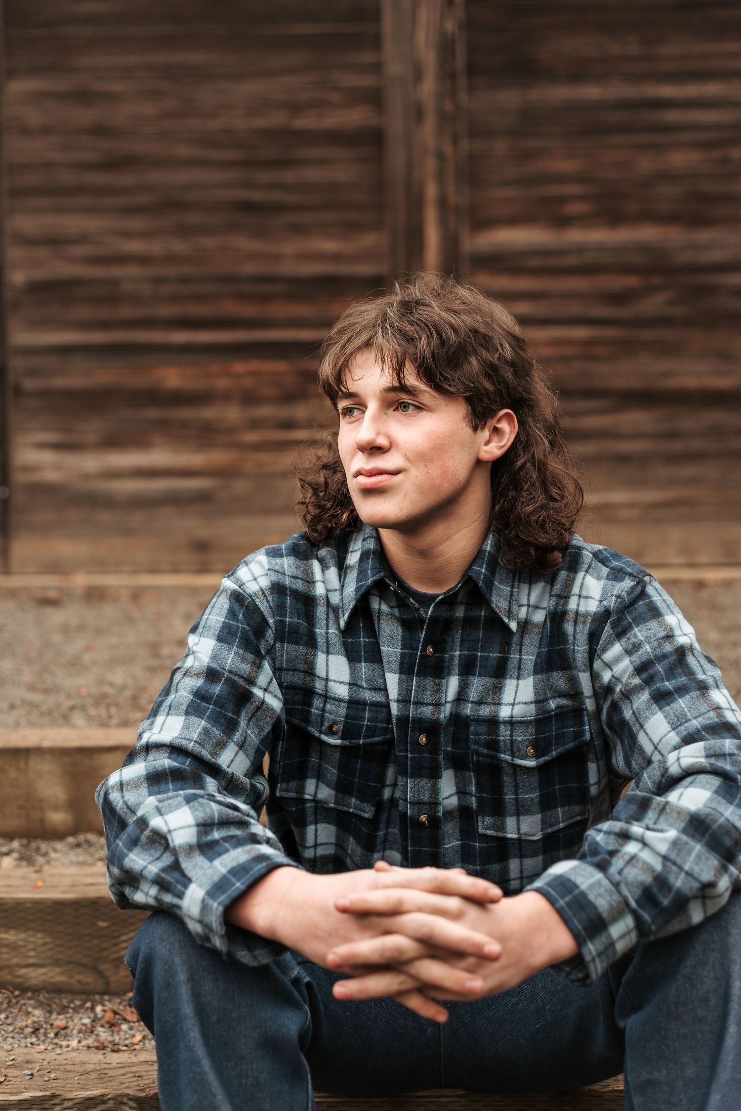 Person in plaid flannel shirt sits on wooden steps with rustic background.