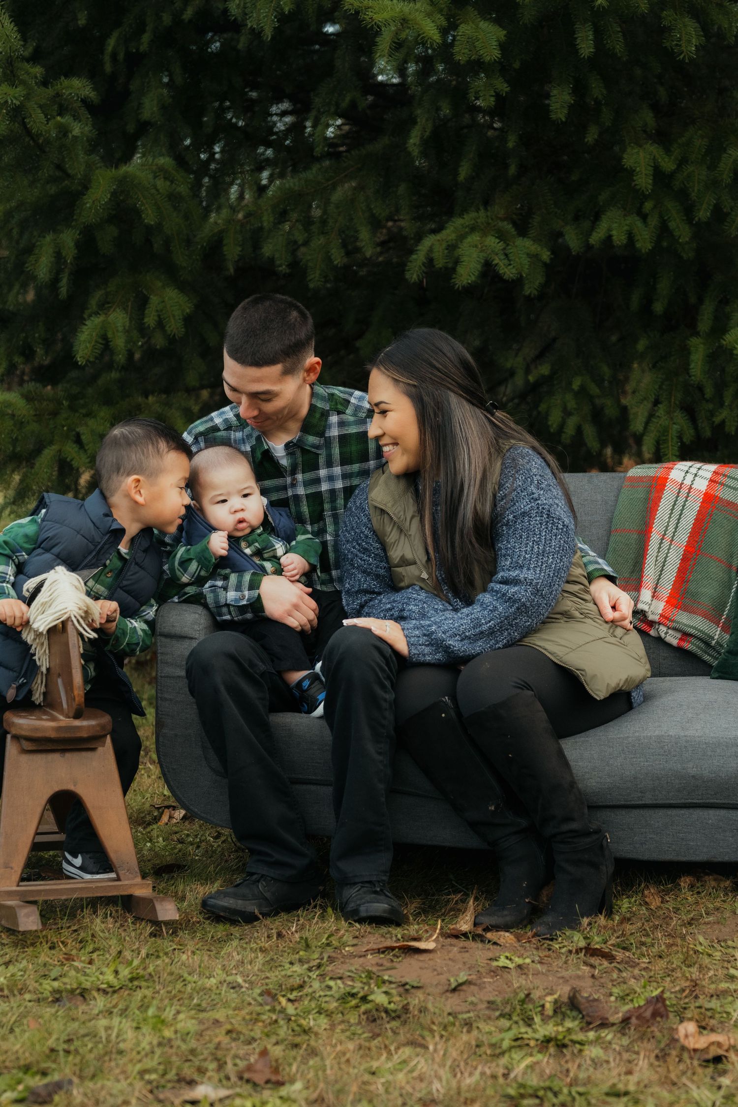 Family shares intimate moment while relaxing on outdoor couch against evergreen trees.