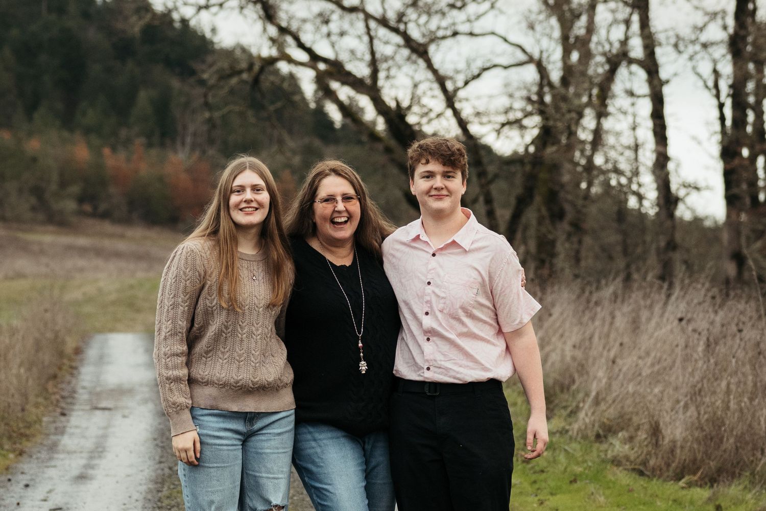 Three smiling women walking together on a rural path surrounded by trees and greenery.