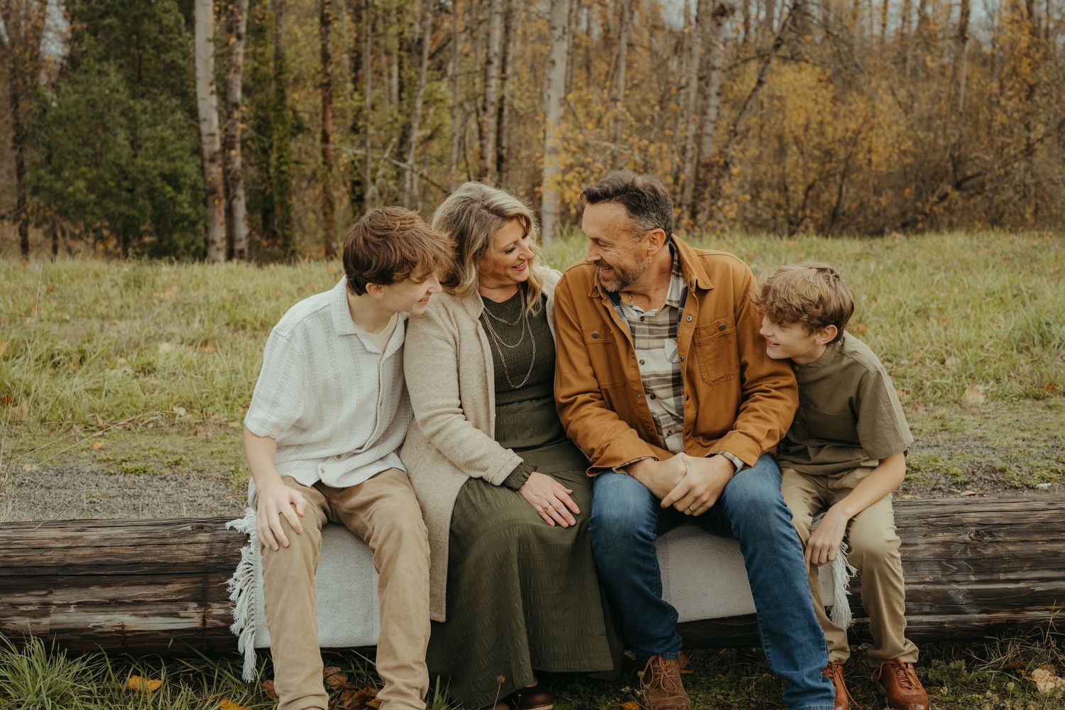 Family sitting together on rustic log bench during fall photo session.