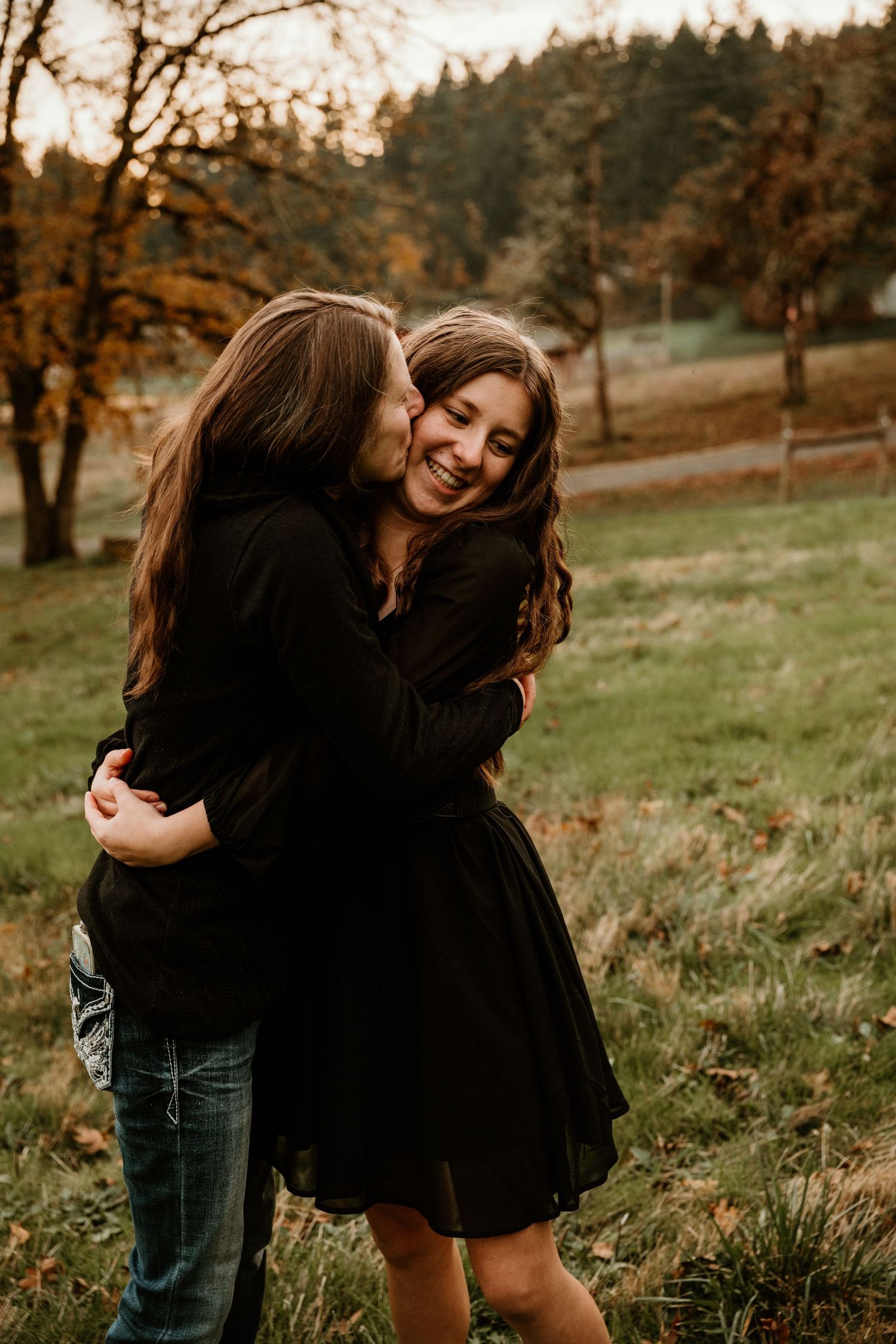 A couple embraces joyfully in a scenic autumn field with trees in the background during golden hour.