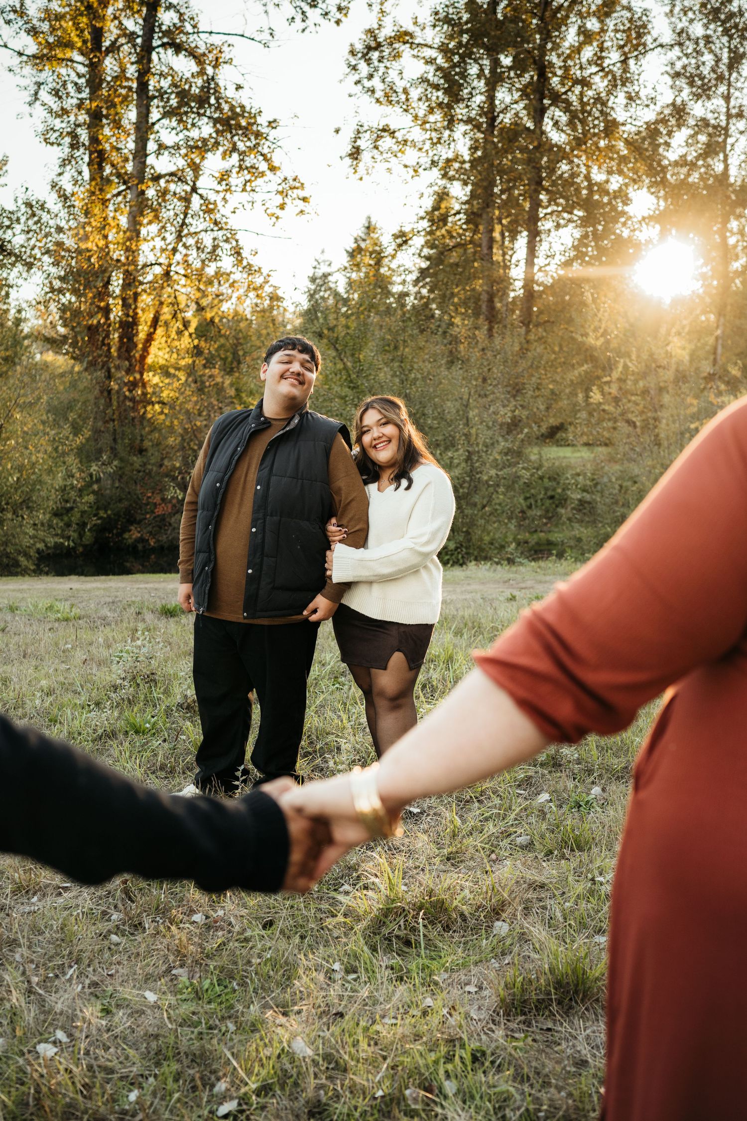 Couple embracing in a sunlit autumn meadow, smiling joyfully, with golden trees and warm sunset light in the background.