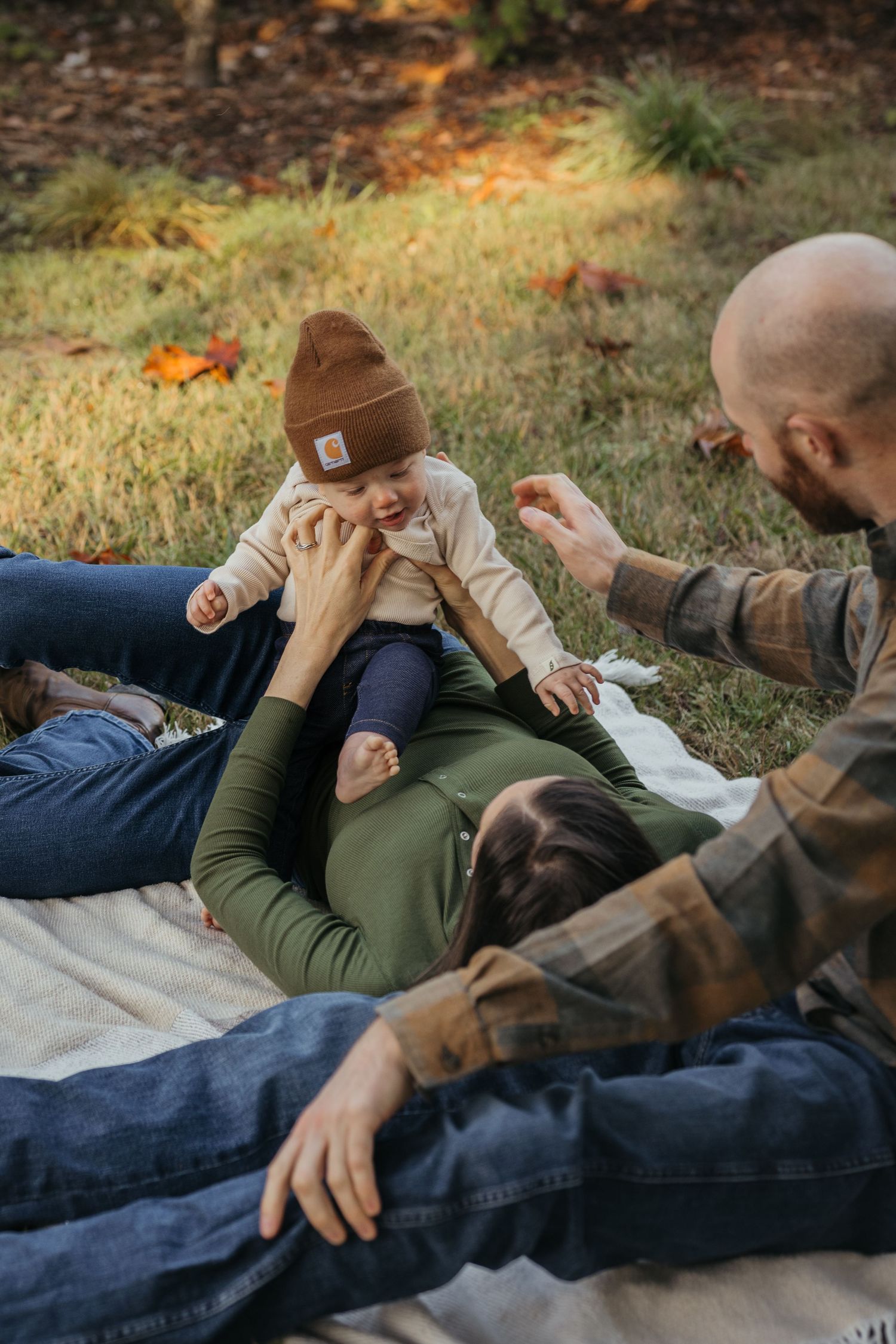 Family shares playful moment while relaxing on blanket during fall photoshoot.
