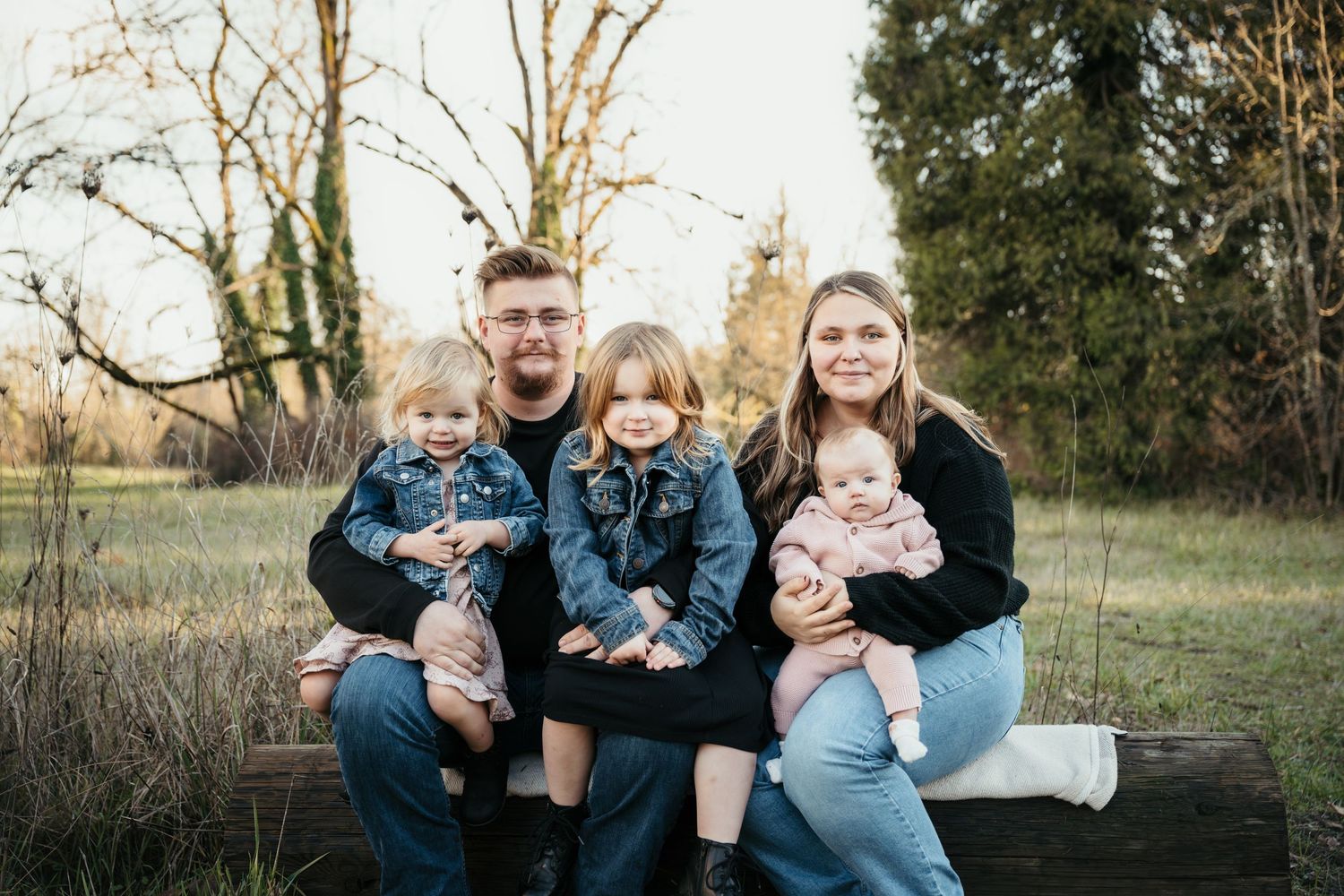 A family sits together on a rustic wooden bench in an outdoor setting during golden hour.