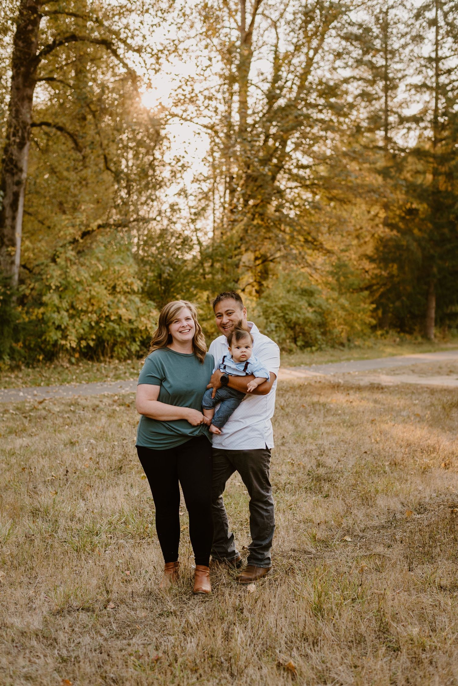 Family enjoying a sunny autumn day together on a trail surrounded by tall trees and golden grass.