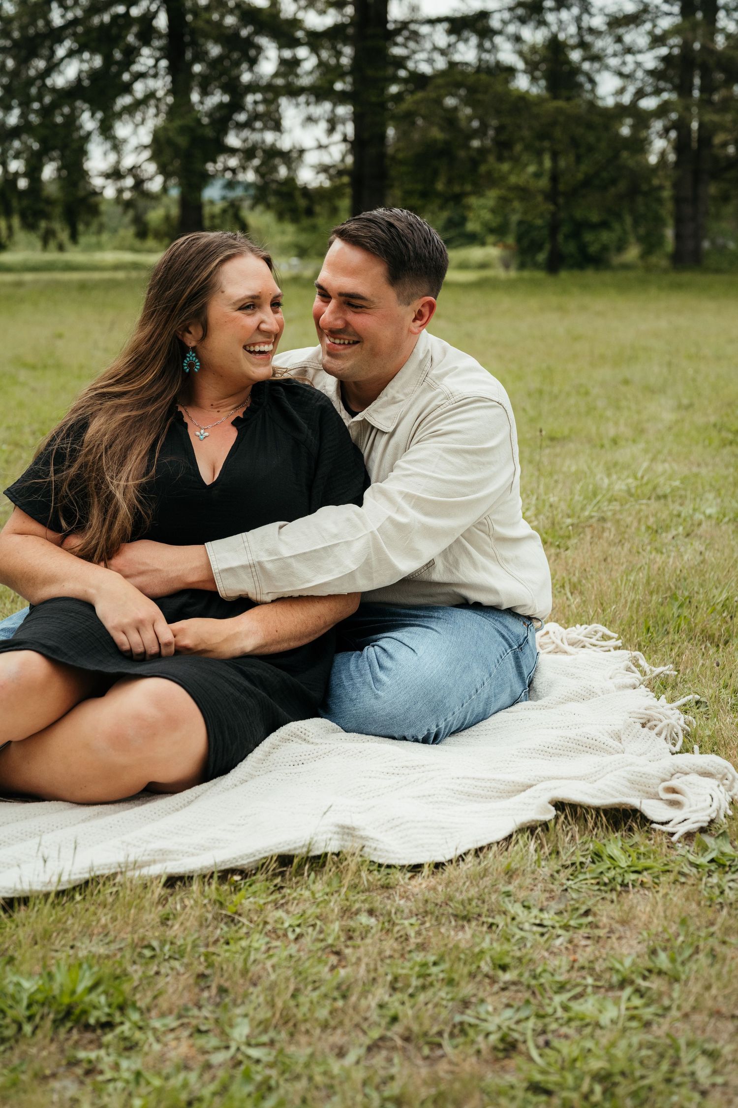 A couple shares a joyful moment while sitting together on a white blanket in a grassy field.