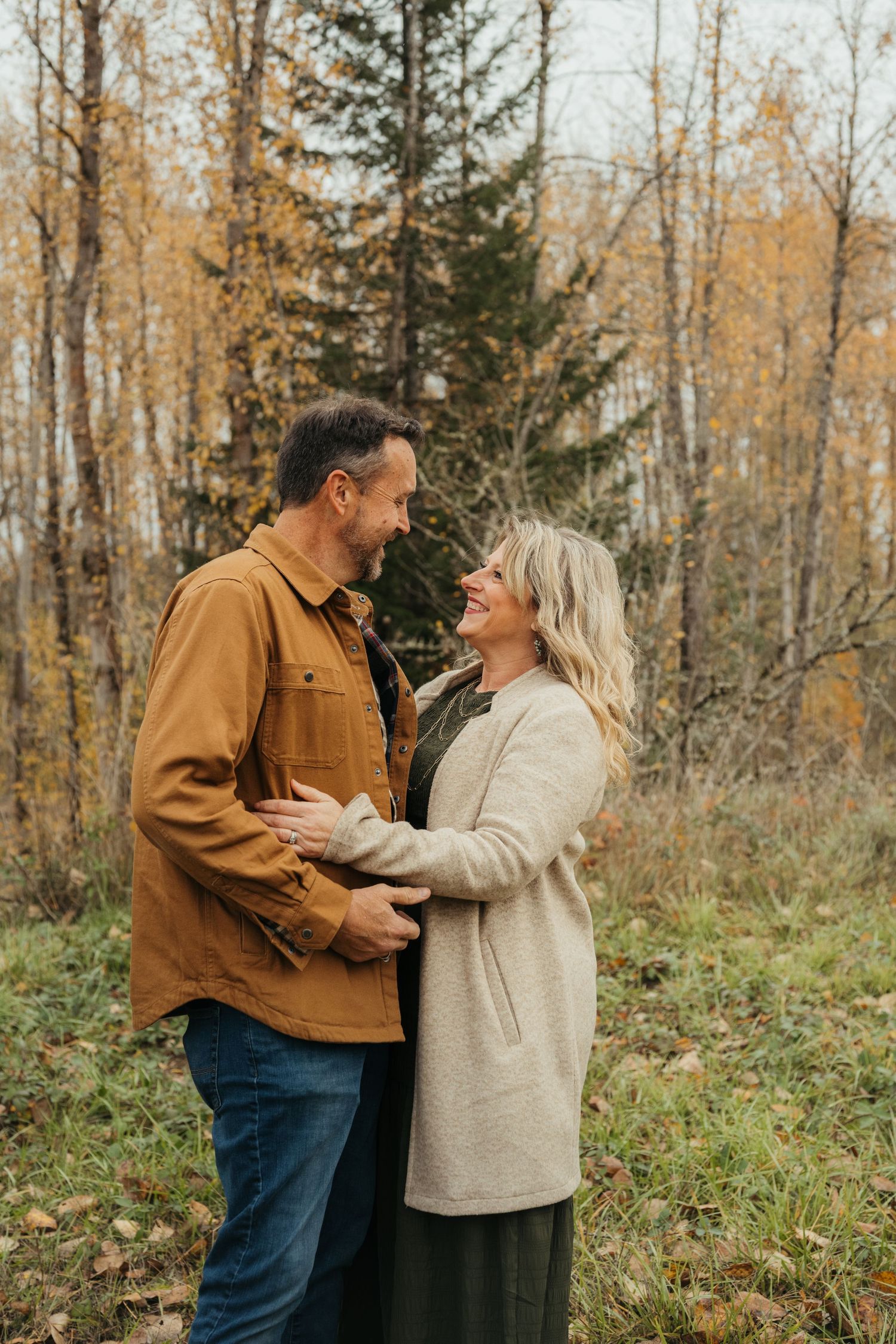 A couple shares a joyful moment together in a forest during fall season.