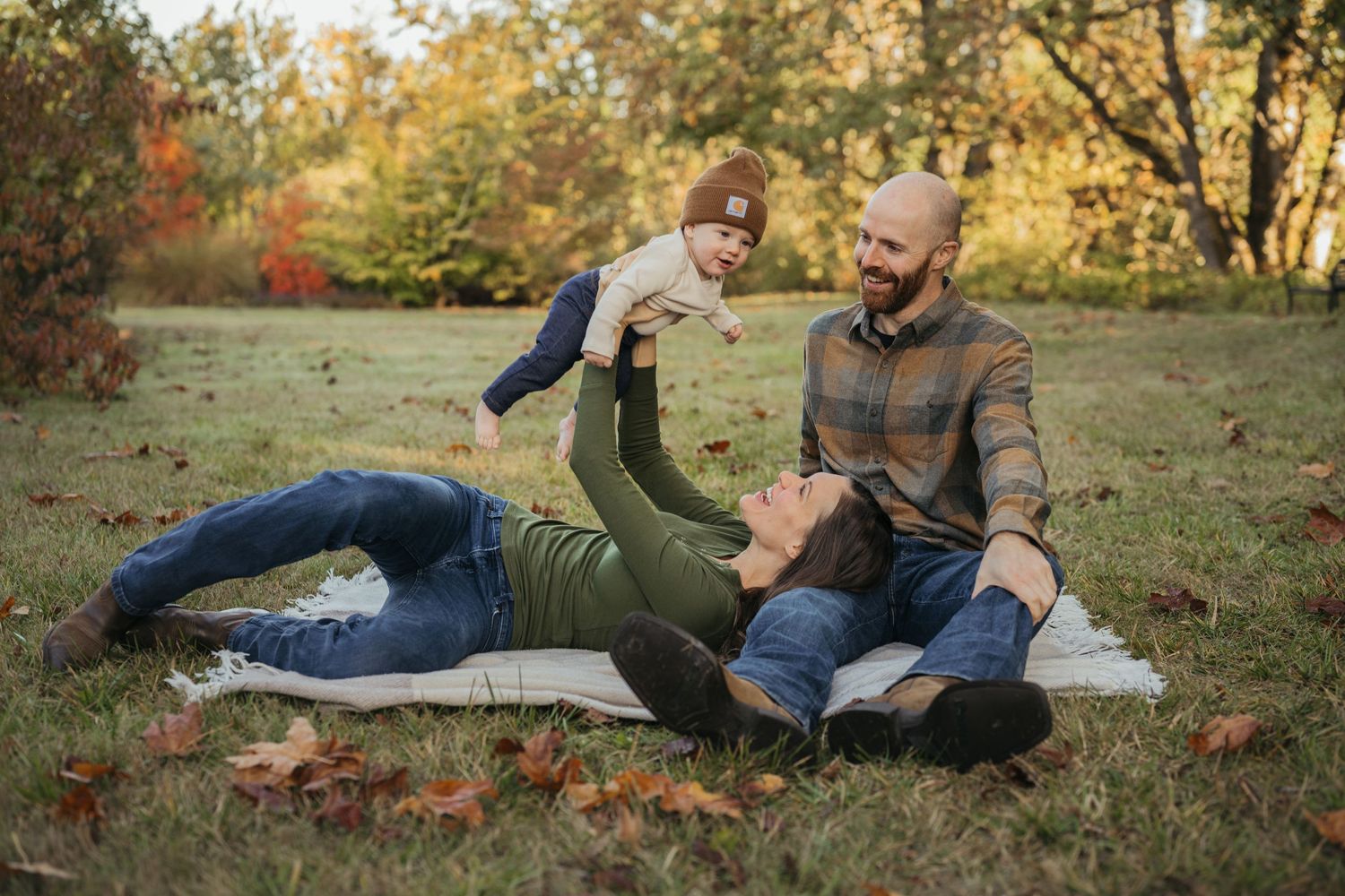 Two people sitting on a blanket outdoors enjoying a playful moment together in autumn foliage.