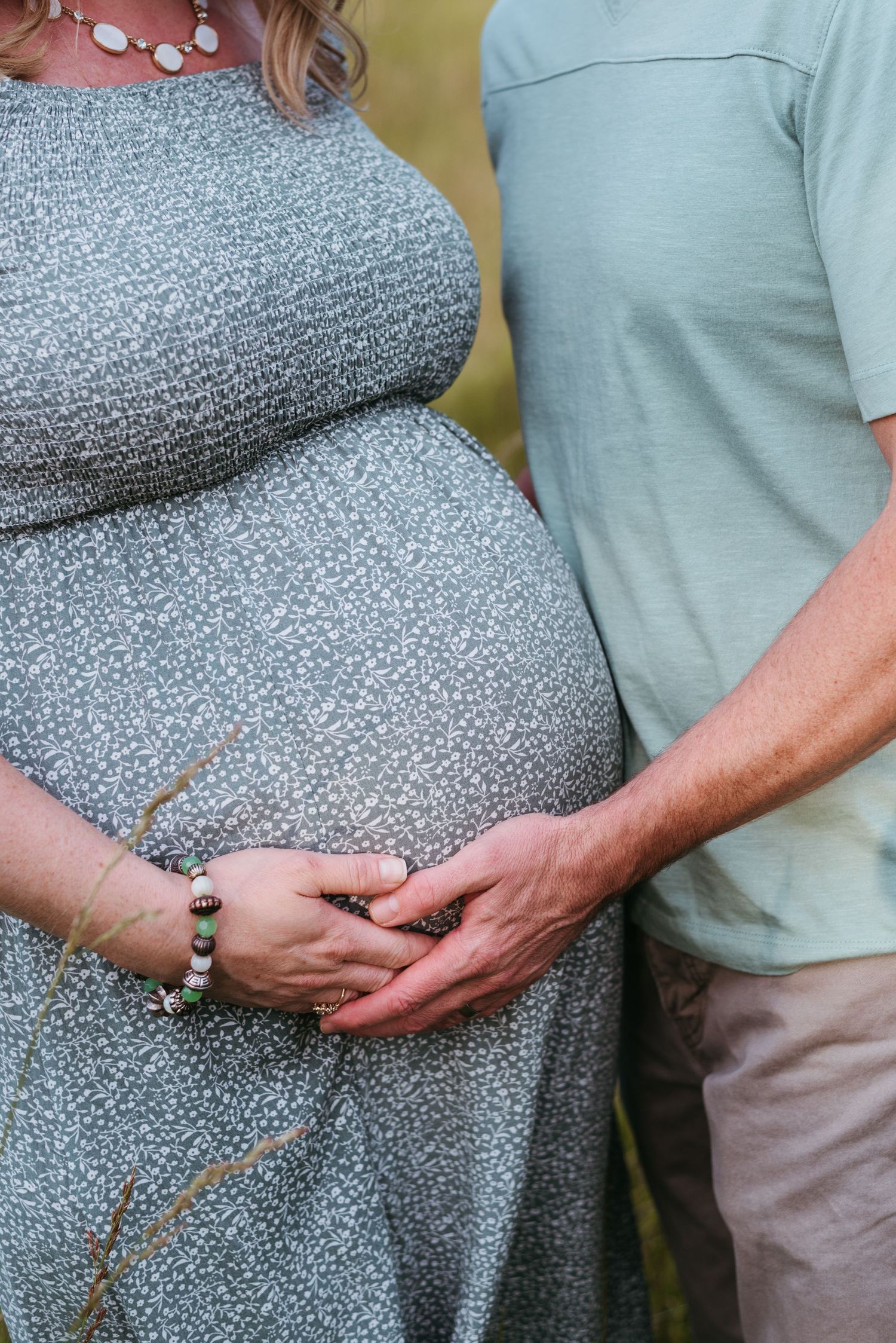 Close-up of pregnant belly with hands tenderly placed on gray textured dress.
