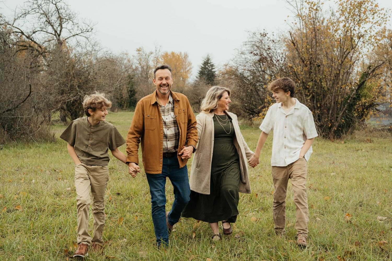 Family walking together hand in hand through autumn field with golden light.