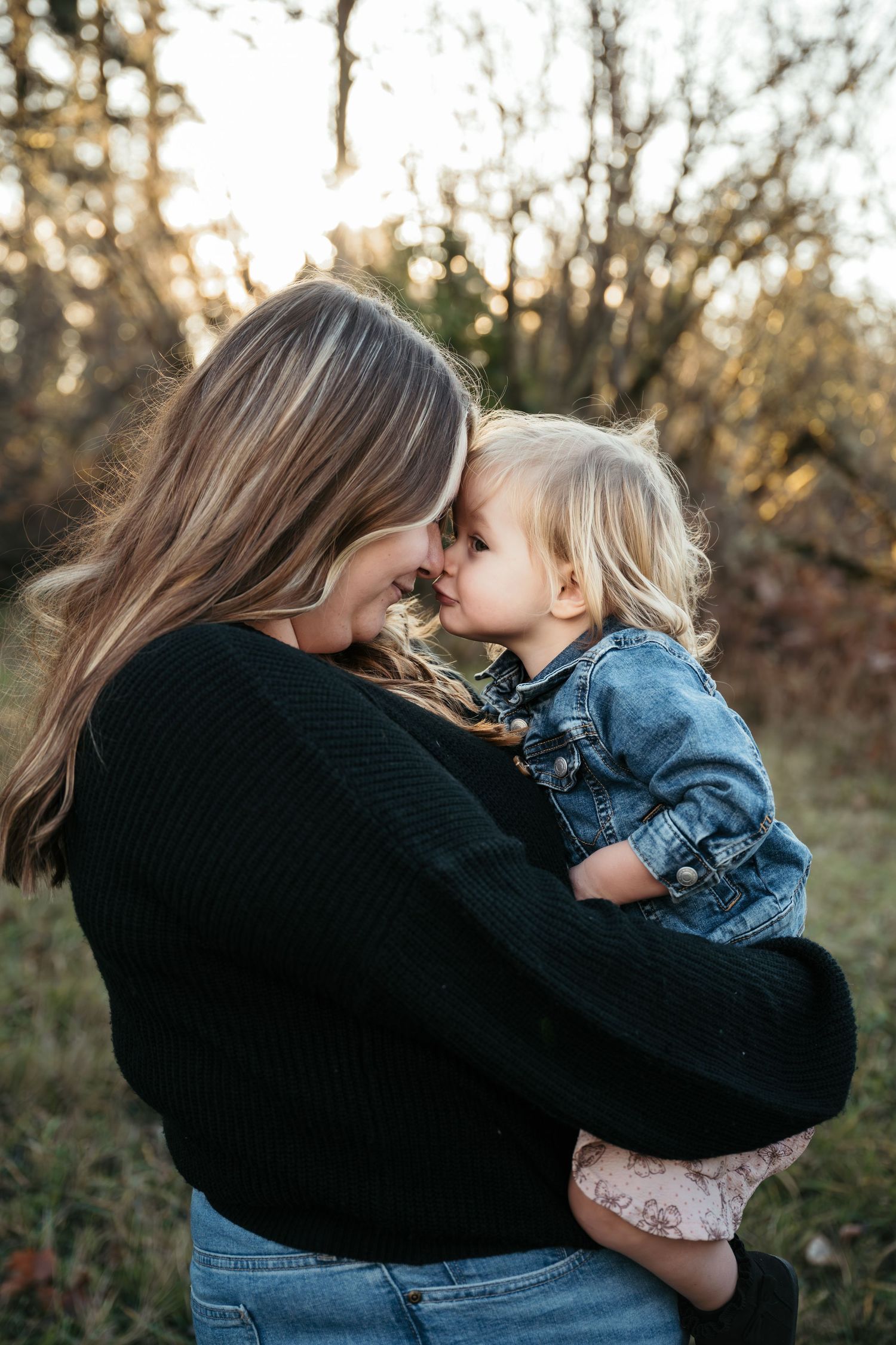 A mother holding her toddler close, touching foreheads in a tender moment outdoors during golden hour.