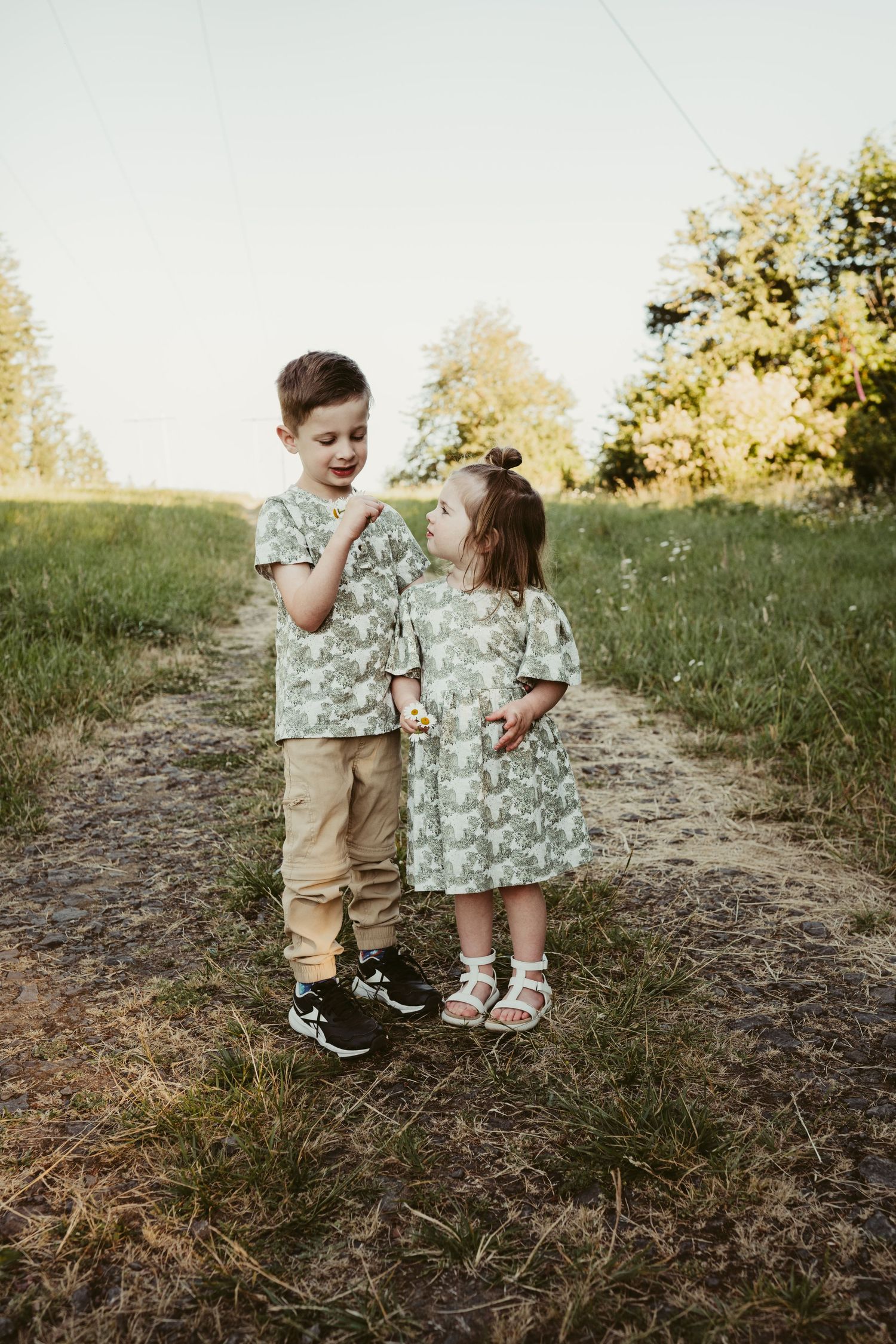Two children in matching outfits sharing a sweet moment on country path.