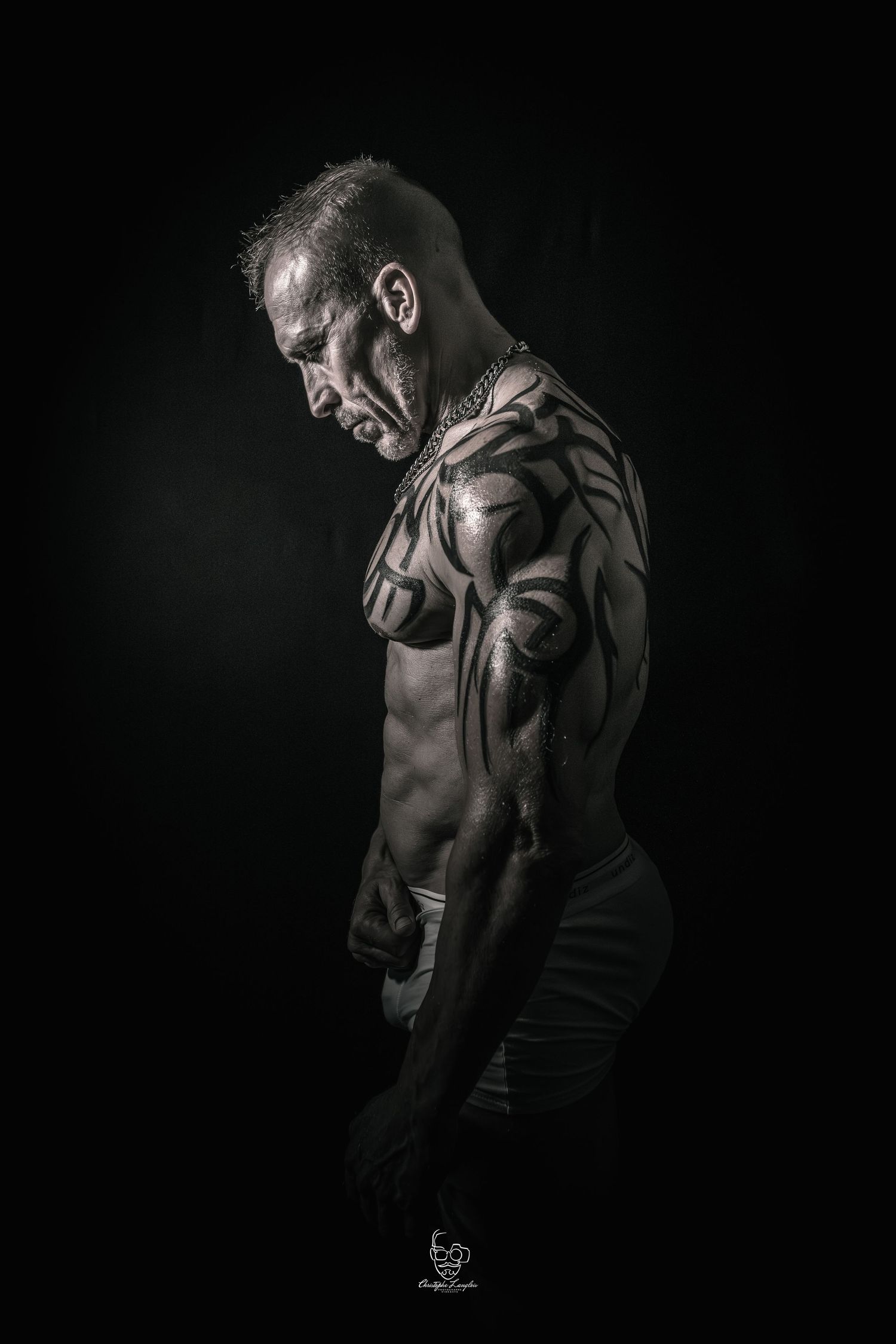 Dramatic black and white artistic portraits showing a muscular torso in moody lighting against dark background.