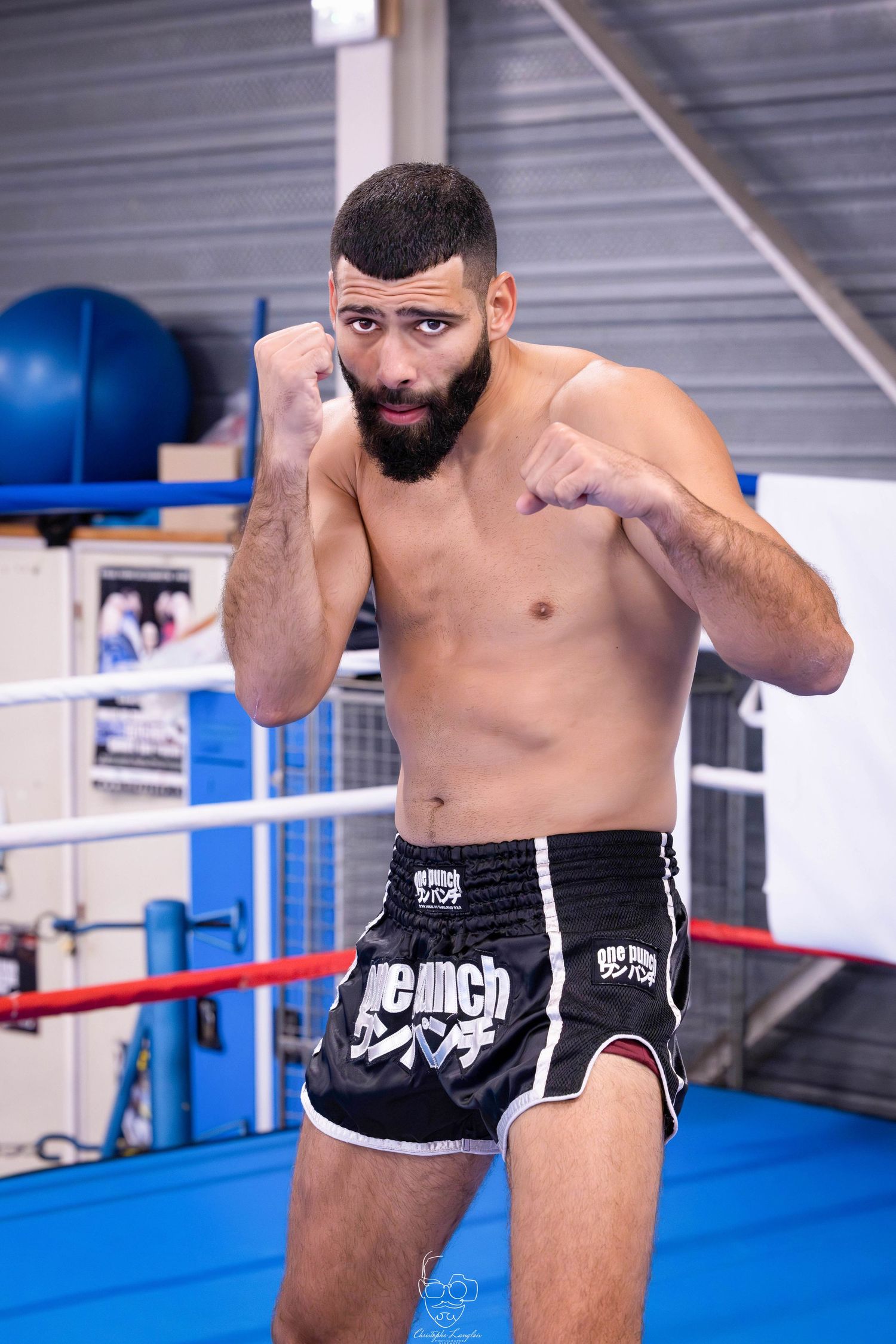Boxer in fighting stance wearing black shorts demonstrates defensive posture in boxing ring.