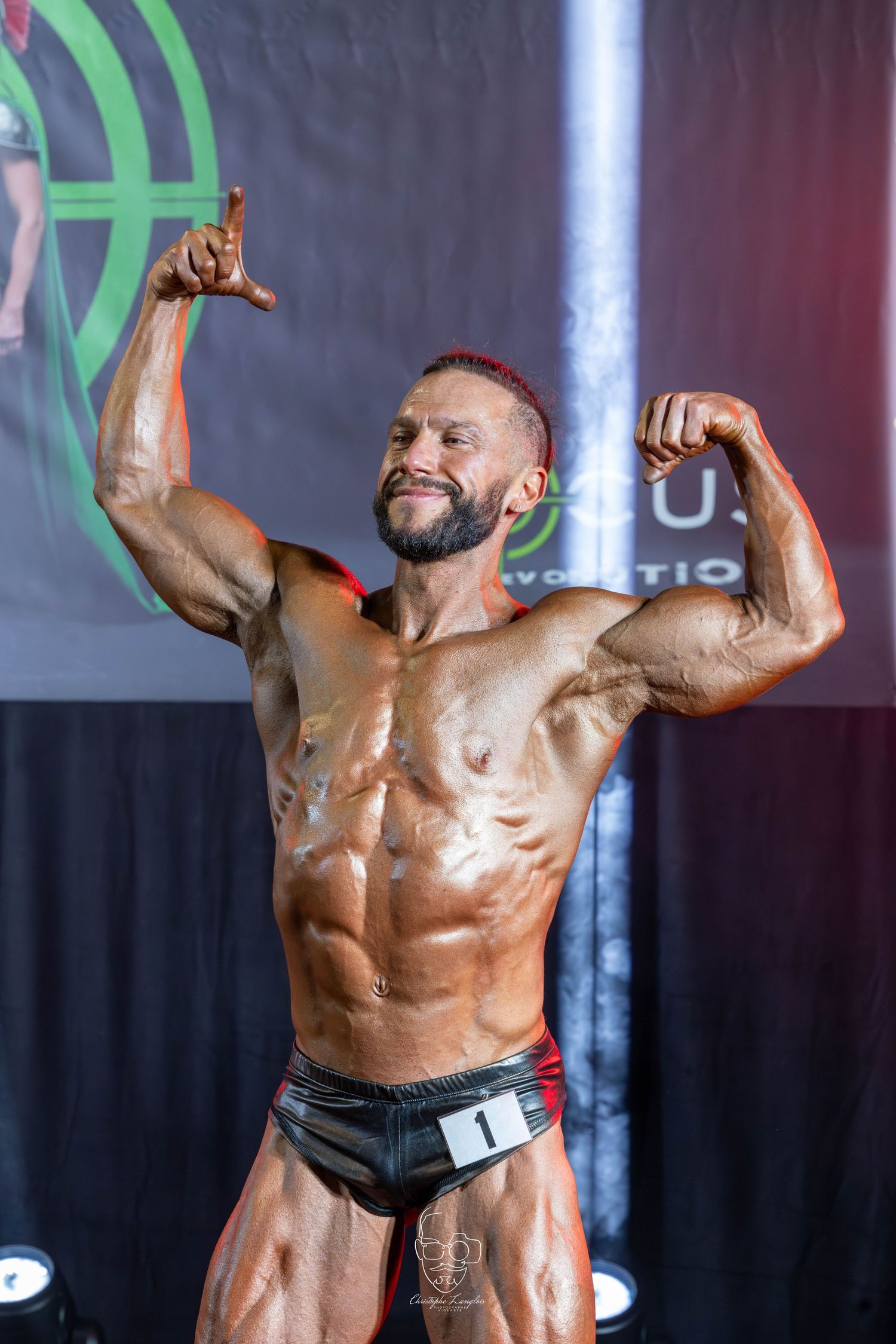 Bodybuilder striking victory pose on stage during competition with dramatic lighting.