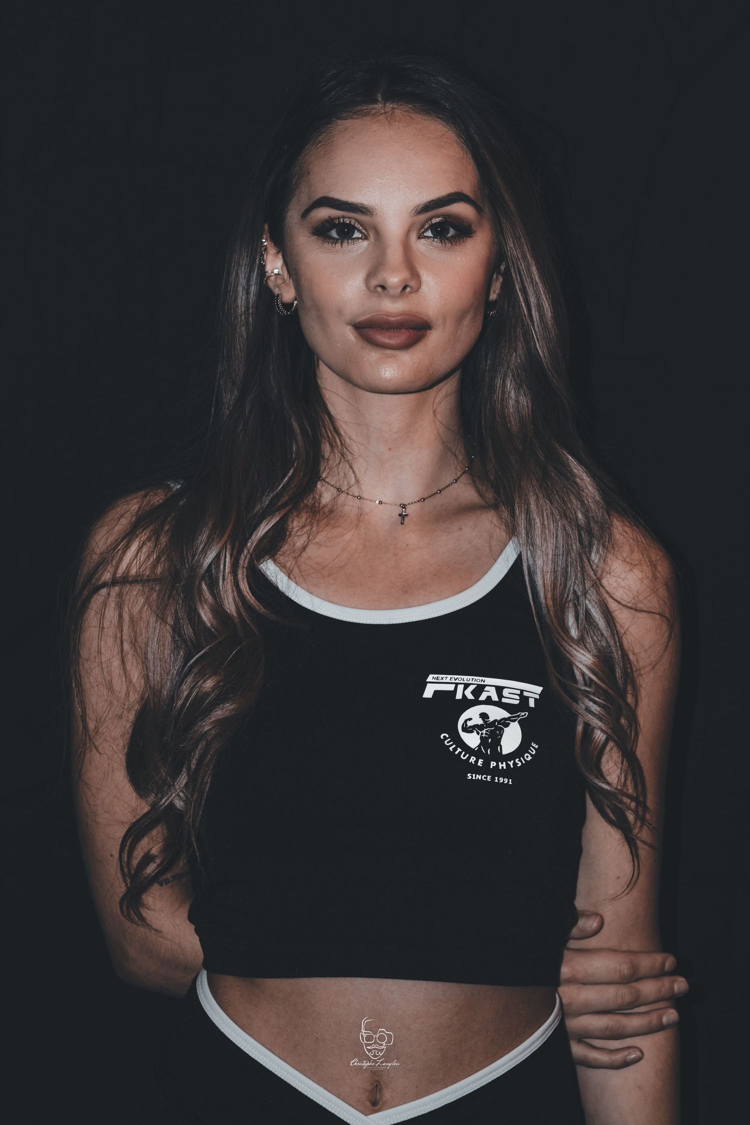 Athletic woman in black sports bra with white trim poses against dark background in fashion photoshoot series.