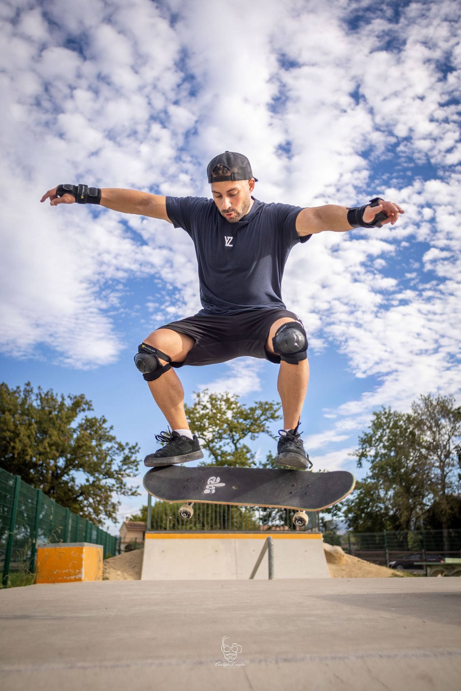 Skateboarder performs an ollie trick sequence at a skate park under cloudy skies.