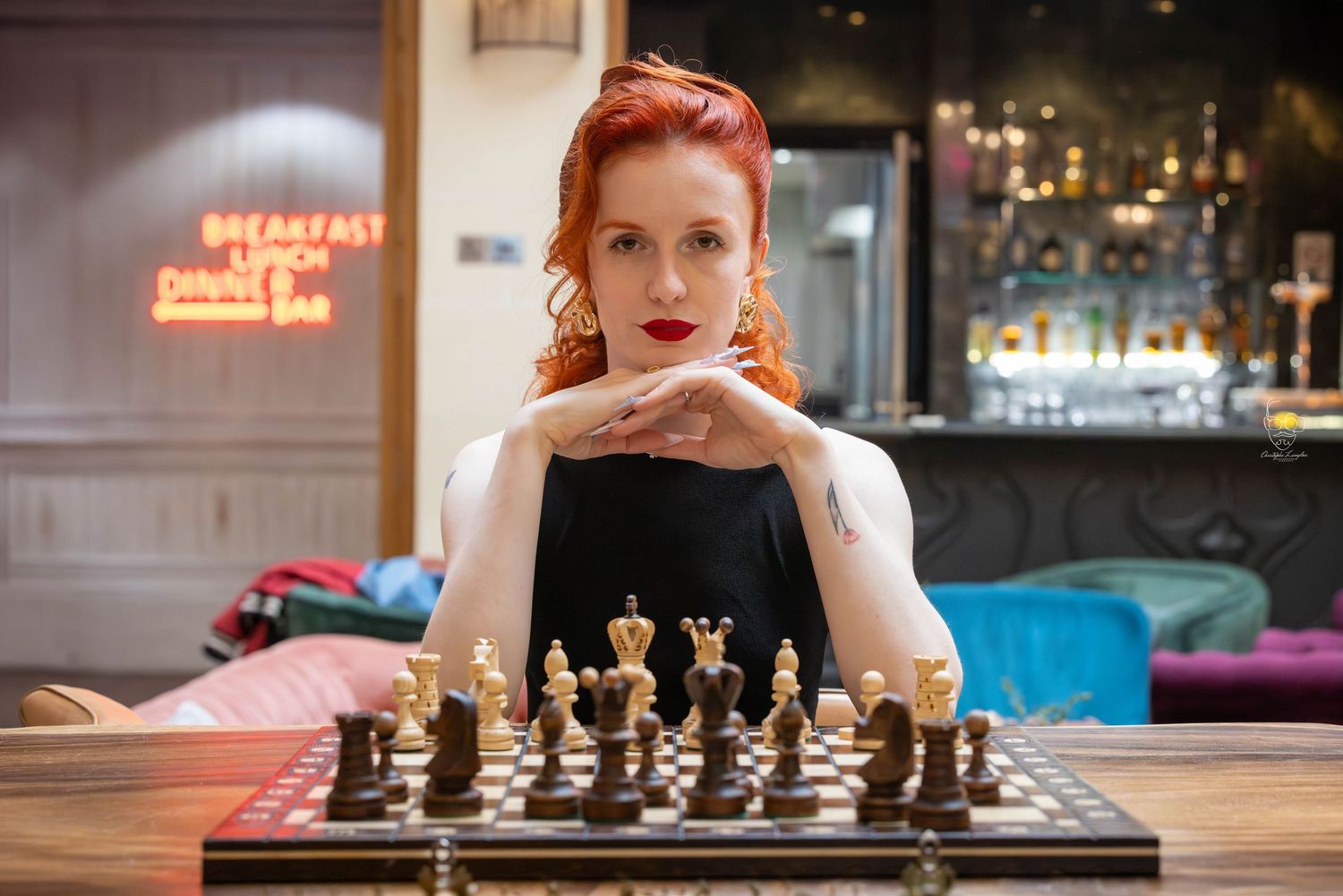 A person contemplates their next move while playing chess at a table in a dimly lit cafe setting.
