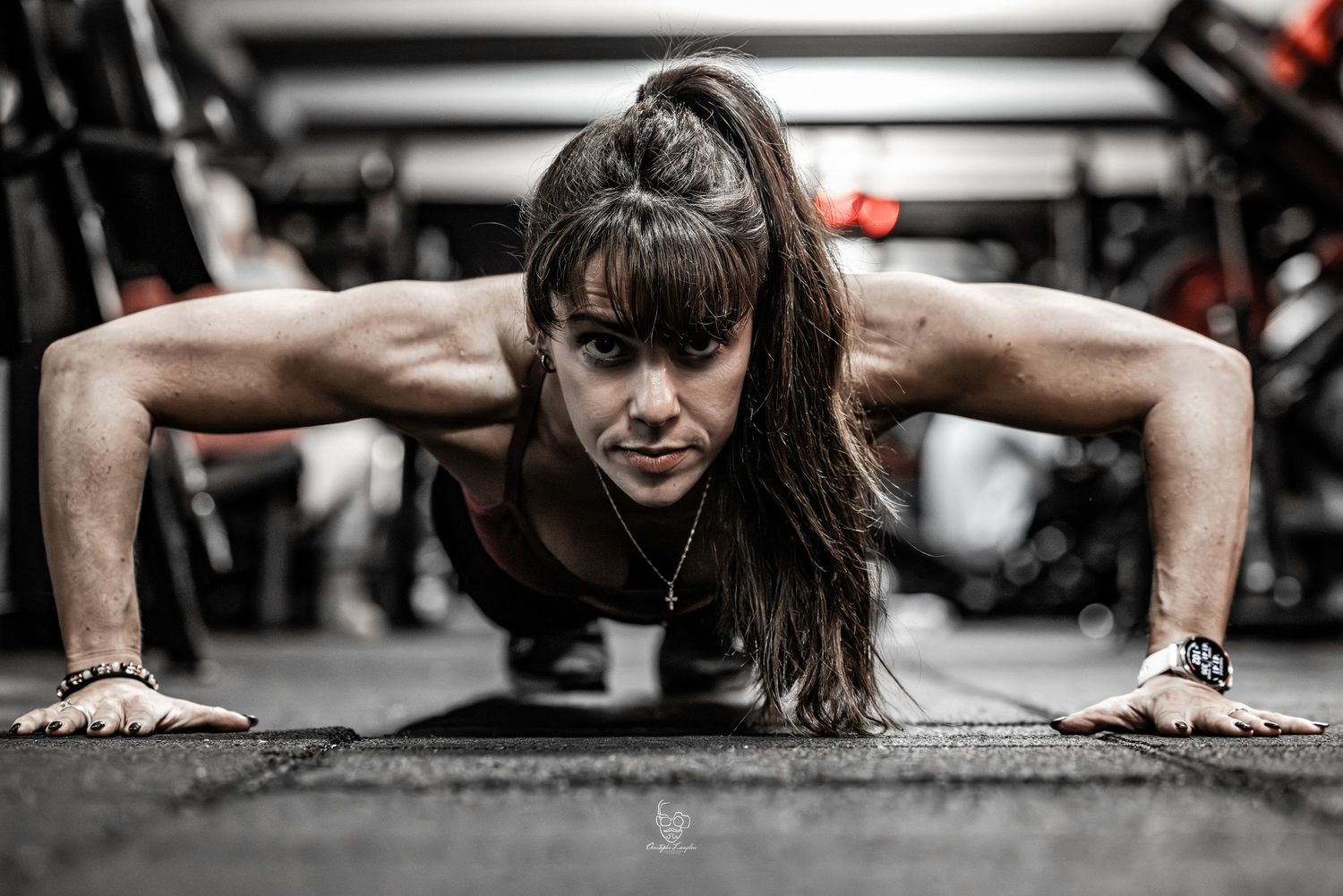 A person performing pushups on a dark floor, shown in a dramatic black and white composition with selective focus.