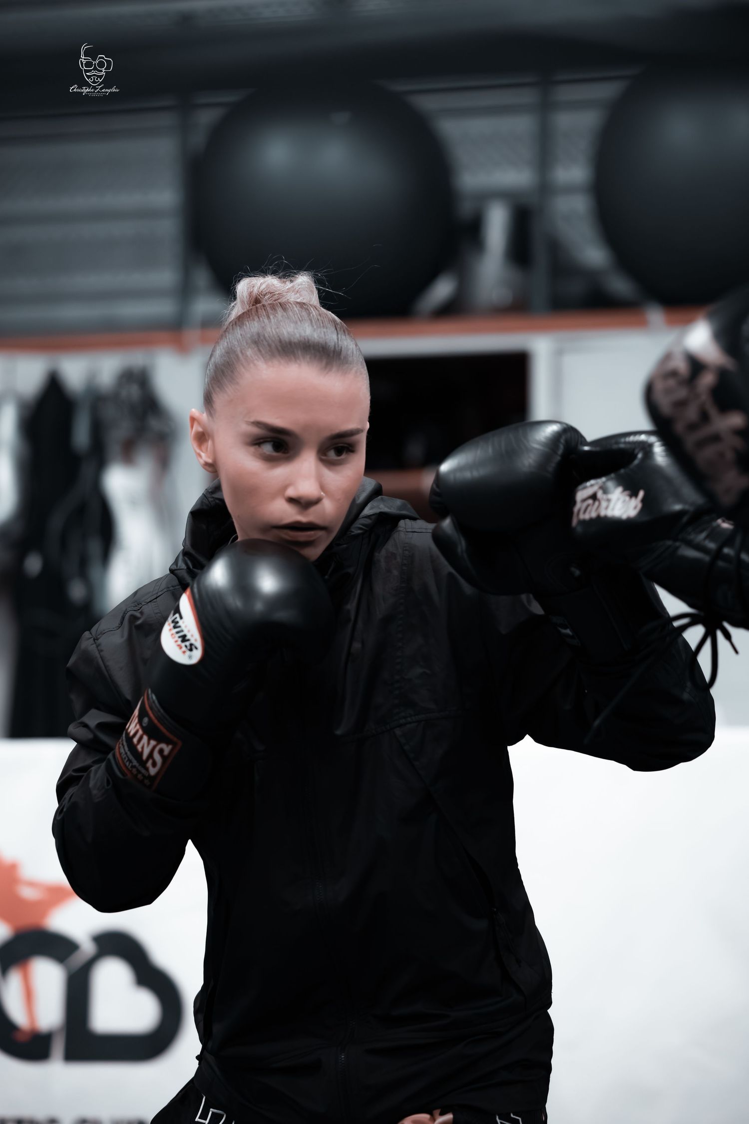 Boxing athlete in black hoodie practicing with gloves in a gym setting.