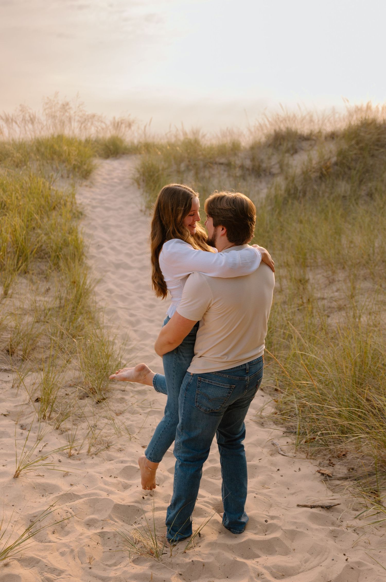 Kayla Ann Photography Sunset Beach Sand Dunes Session Lake Michigan. Couple lift and twirling in the sand with a golden glow from the sun.
