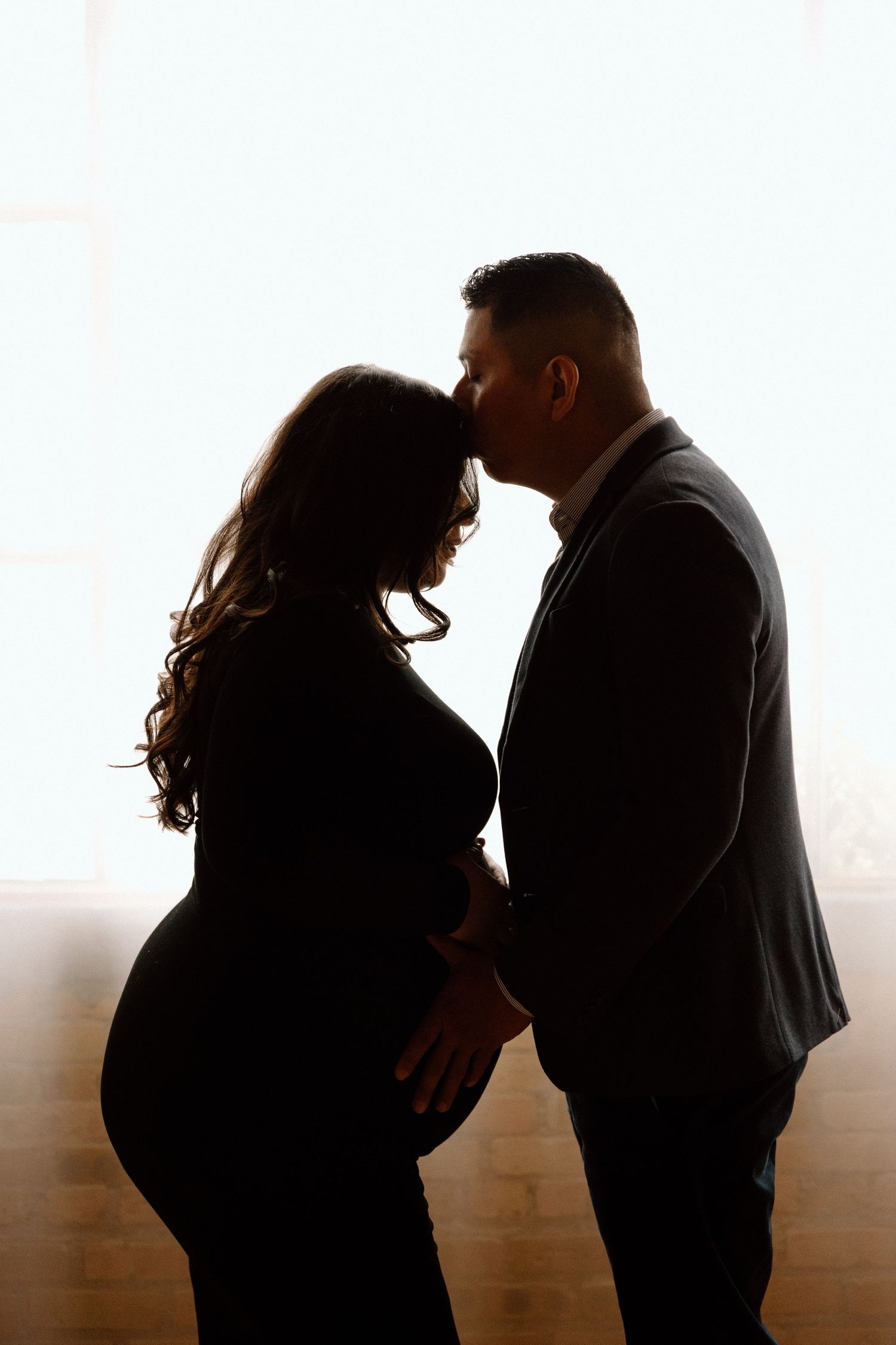 A tender moment as a father-to-be kisses his partner’s forehead during their intimate studio maternity session. Maternity Photographer.